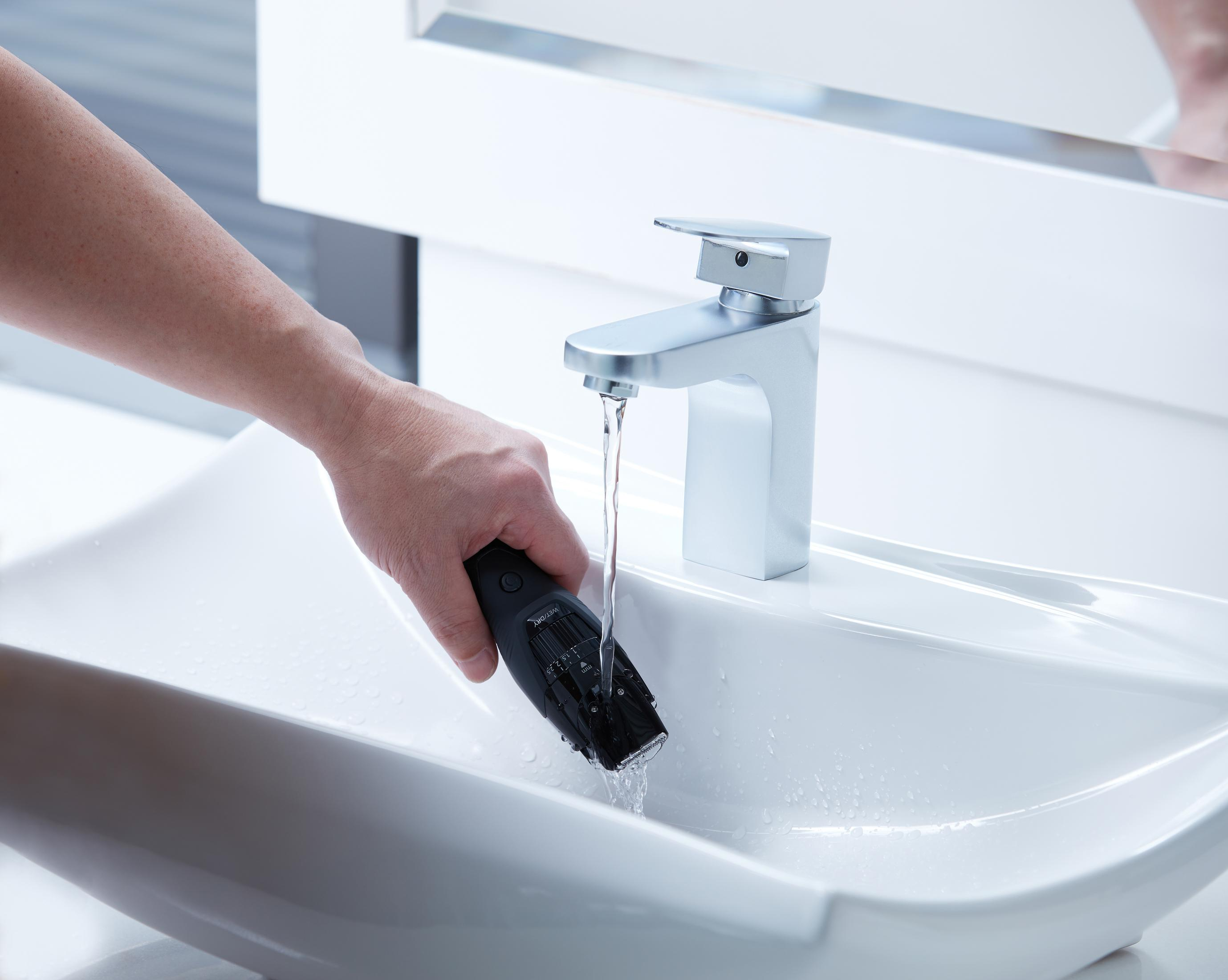 Une personne tenant un rasoir noir sous l'eau courante dans un lavabo blanc dans une salle de bain.