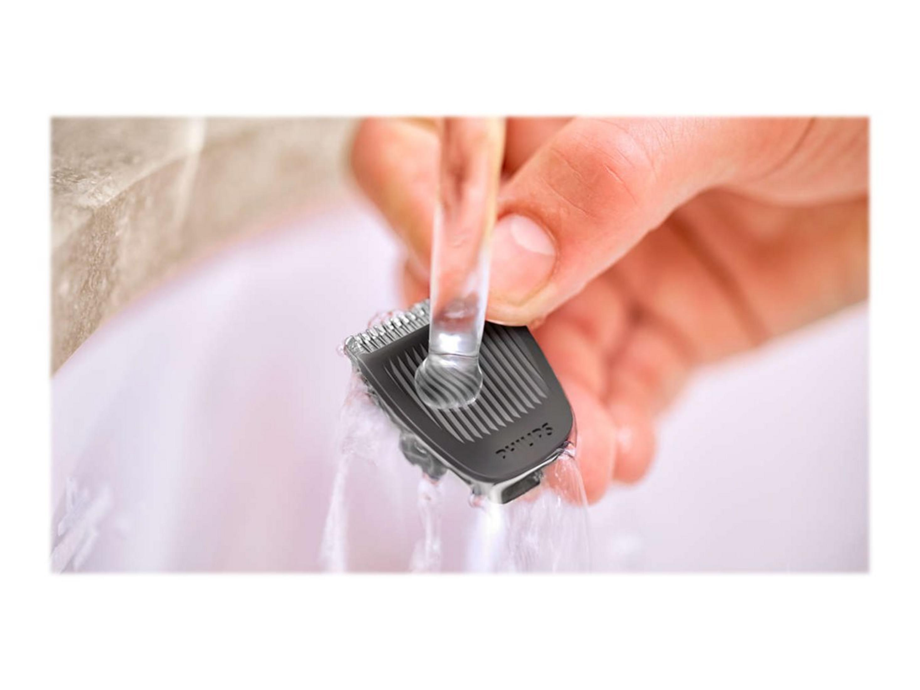 Mano enjuagando un cabezal de afeitadora negro bajo agua corriente en un lavabo blanco.