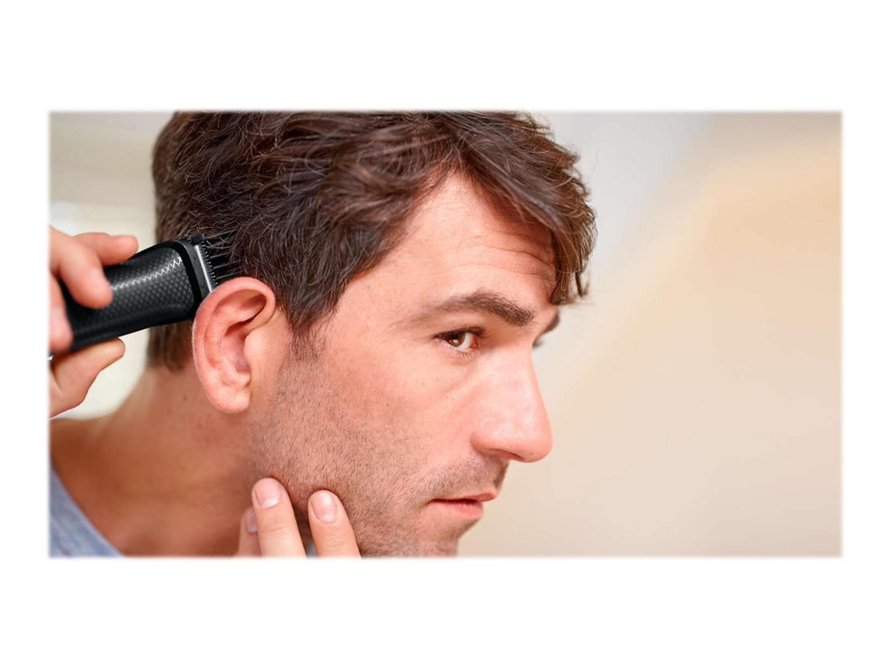 Hombre afeitándose la oreja con una recortadora eléctrica, primer plano de su rostro.