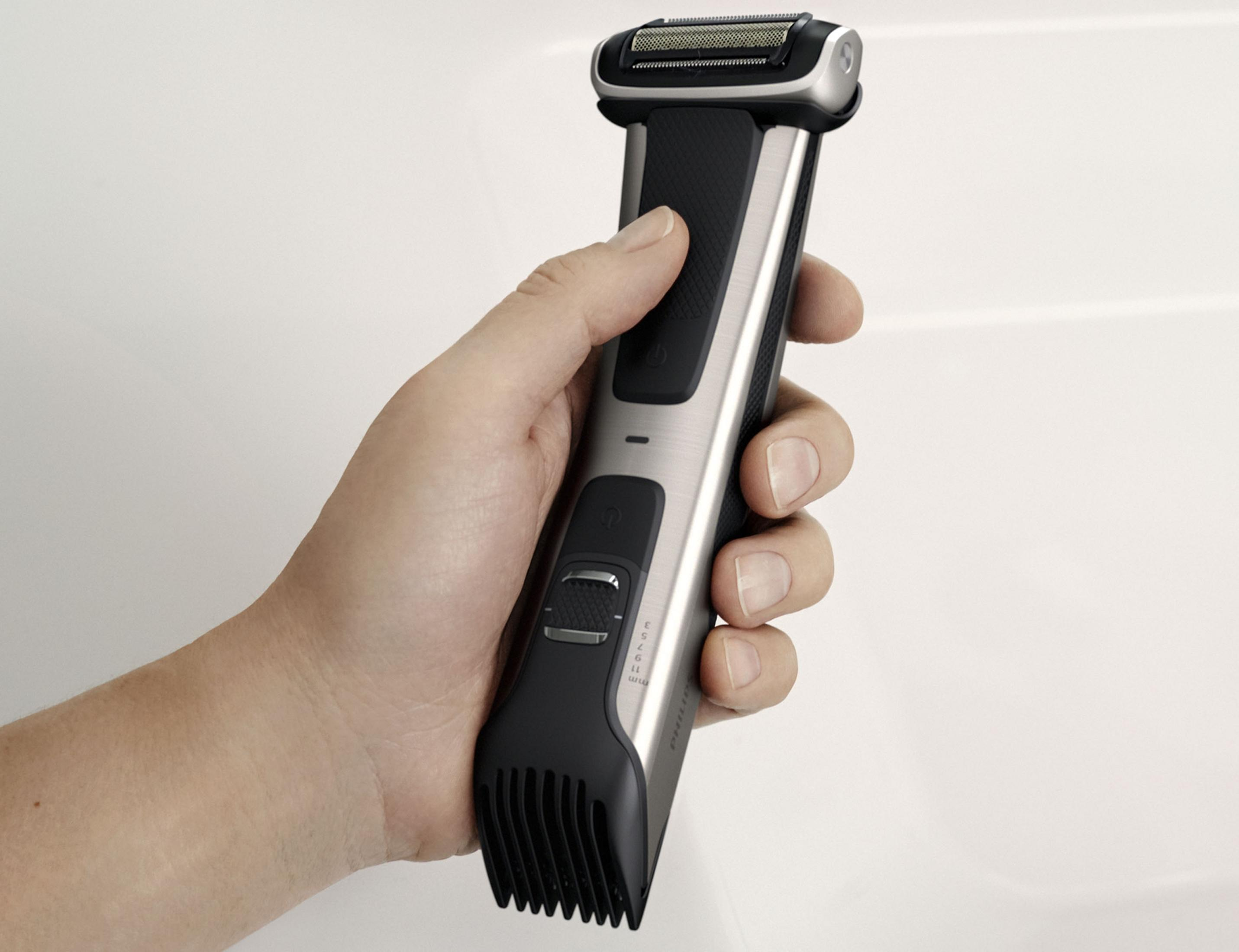 Dłoń trzymająca srebrno-czarny trymer do ciała. Na białym tle.