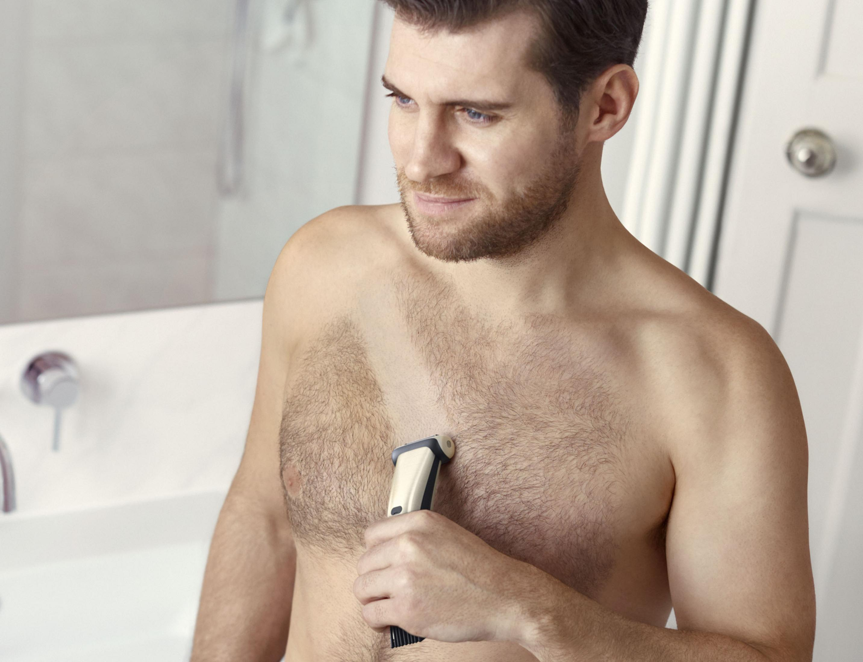 Mężczyzna goli klatkę piersiową trymerem elektrycznym, patrząc w dół.