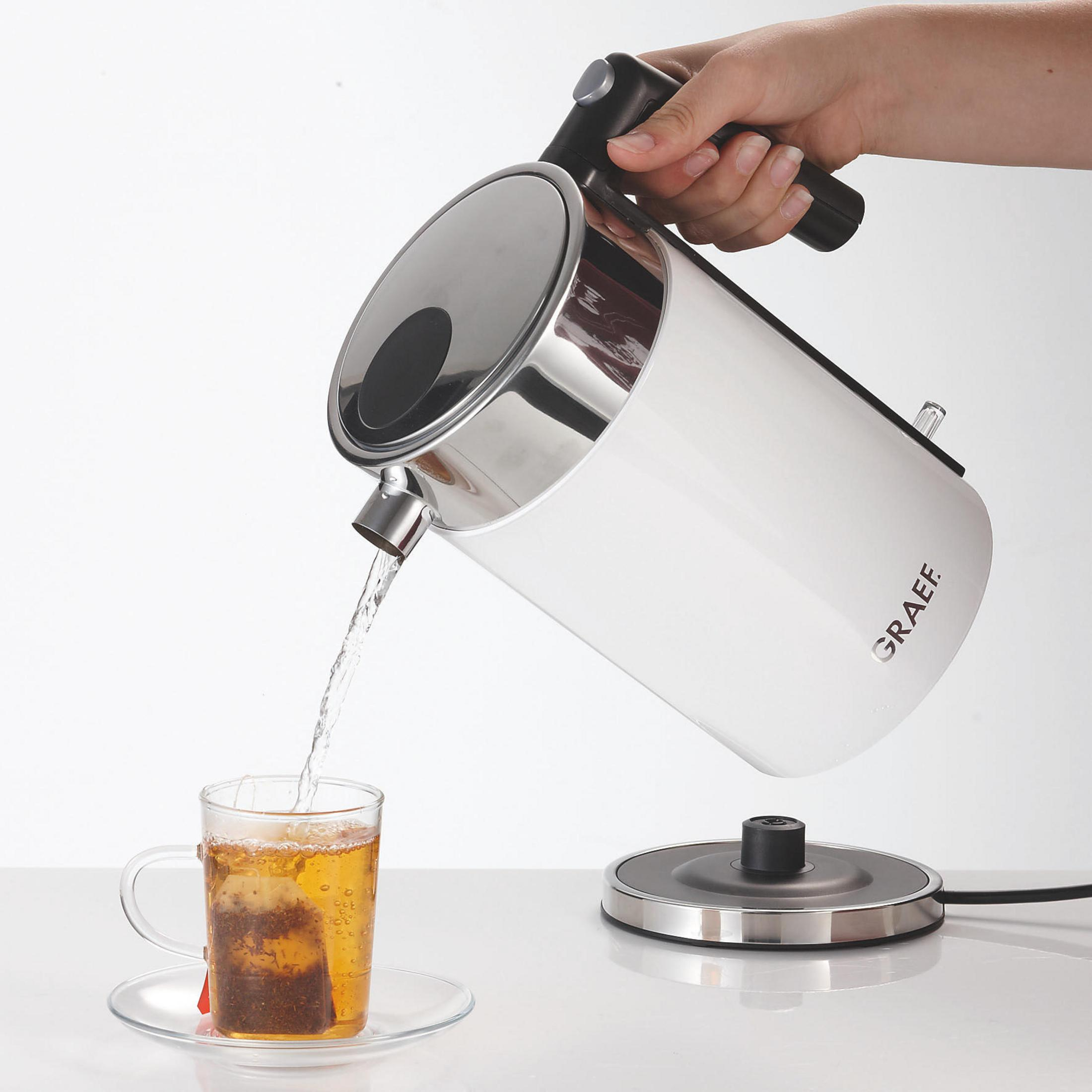 Ein weißer Wasserkocher gießt Wasser in ein Glas Tee. Weißer Hintergrund.