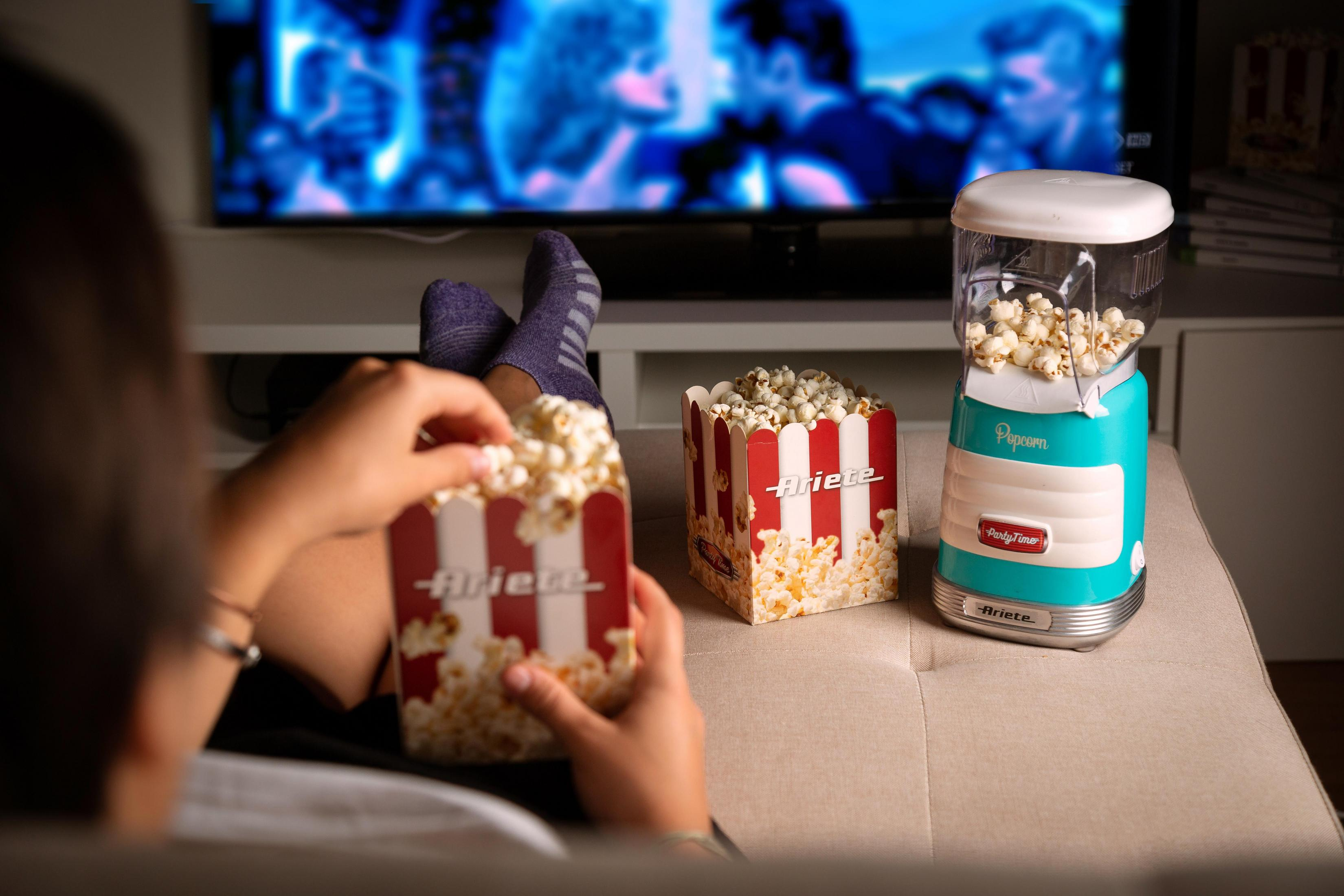 Osoba oglądająca telewizję jedząc popcorn z czerwono-pasiastych pudełek i maszyny do popcornu.