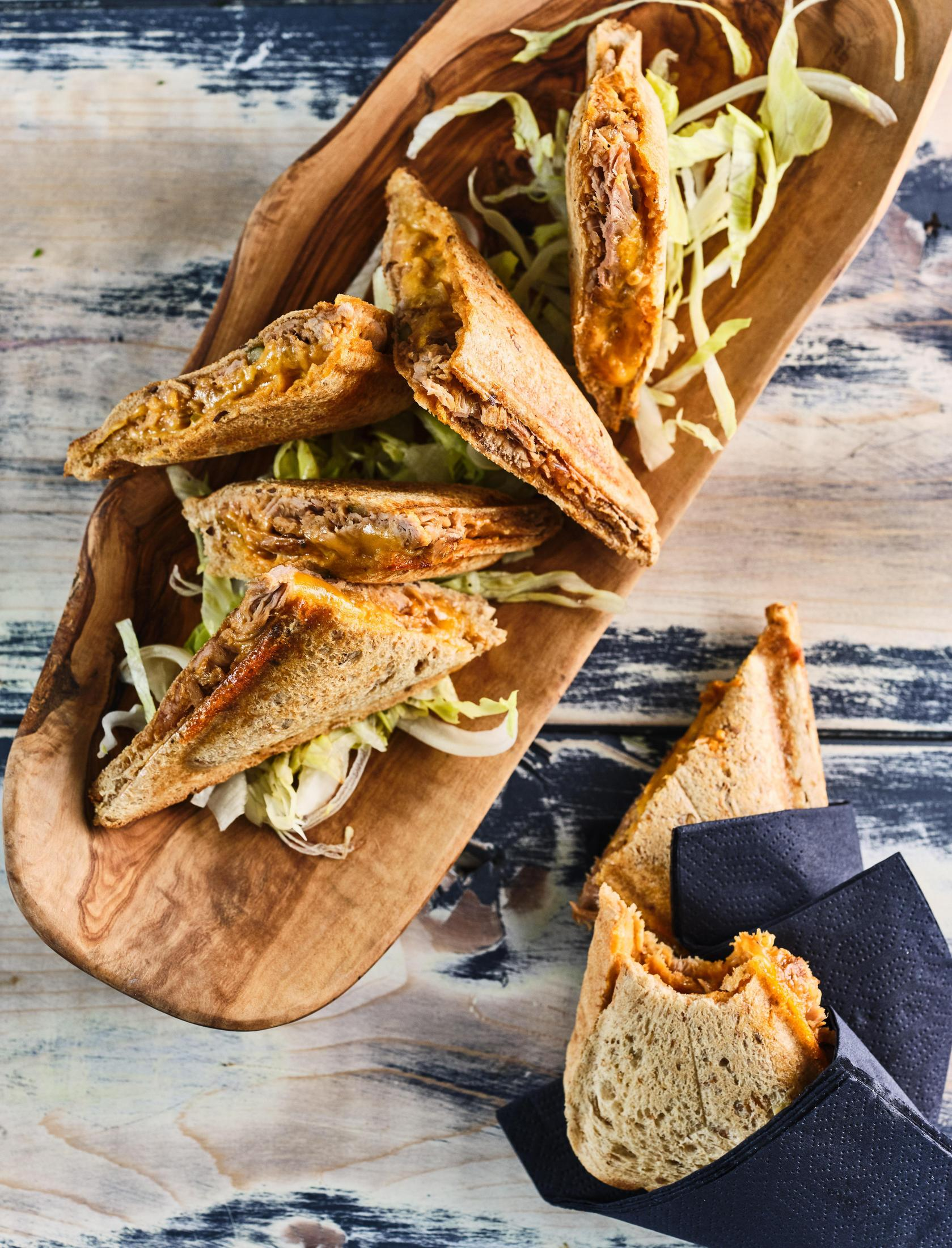 Drewniana deska do serwowania z pokrojonymi kanapkami i sałatką. Kanapki są przekrojone na pół.