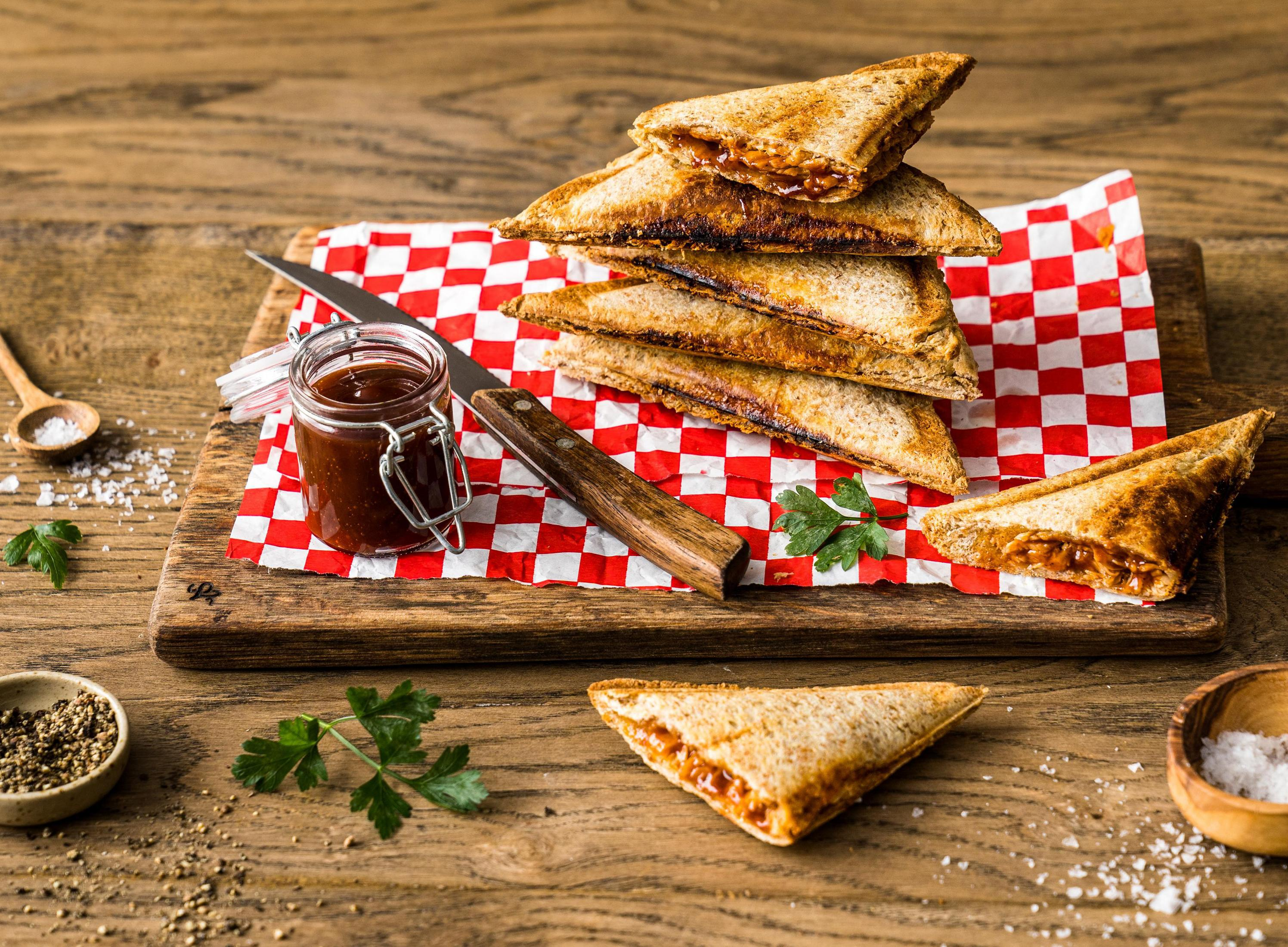 Tostowane kanapki na drewnianej desce ze słoikiem sosu i nożem.