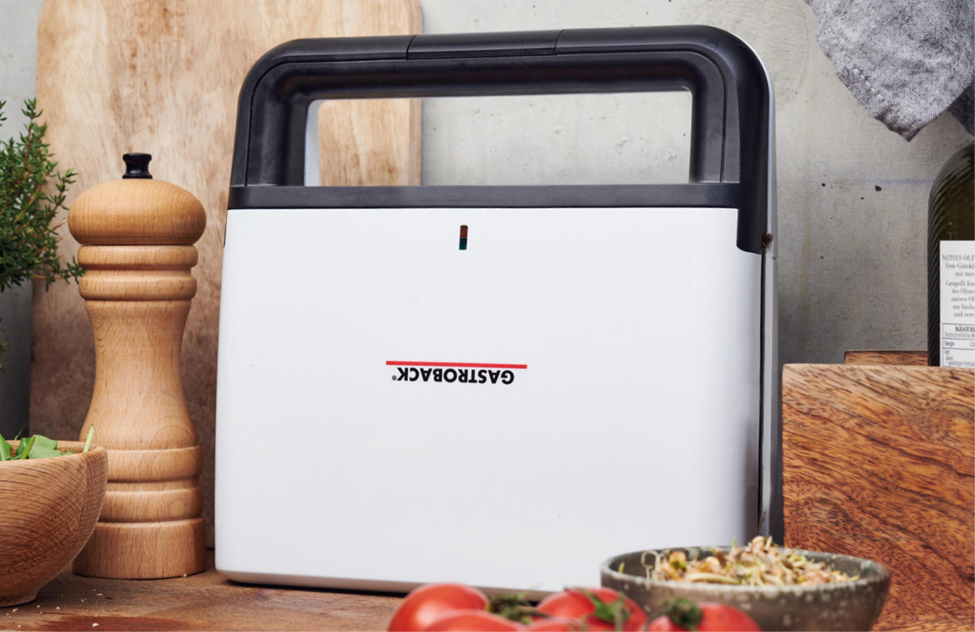 Ein weißer und schwarzer Sandwichmaker auf einer Holzoberfläche mit Zutaten drumherum.