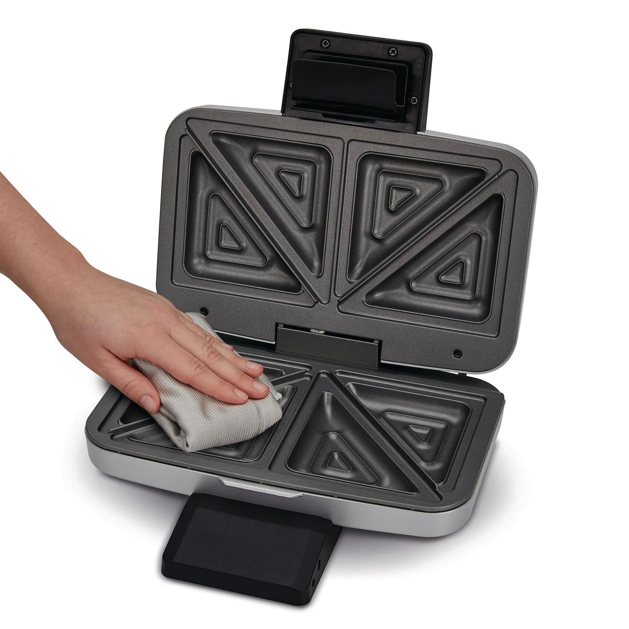 Ręka osoby wycierająca szarą szmatką wnętrze opiekacza do kanapek.