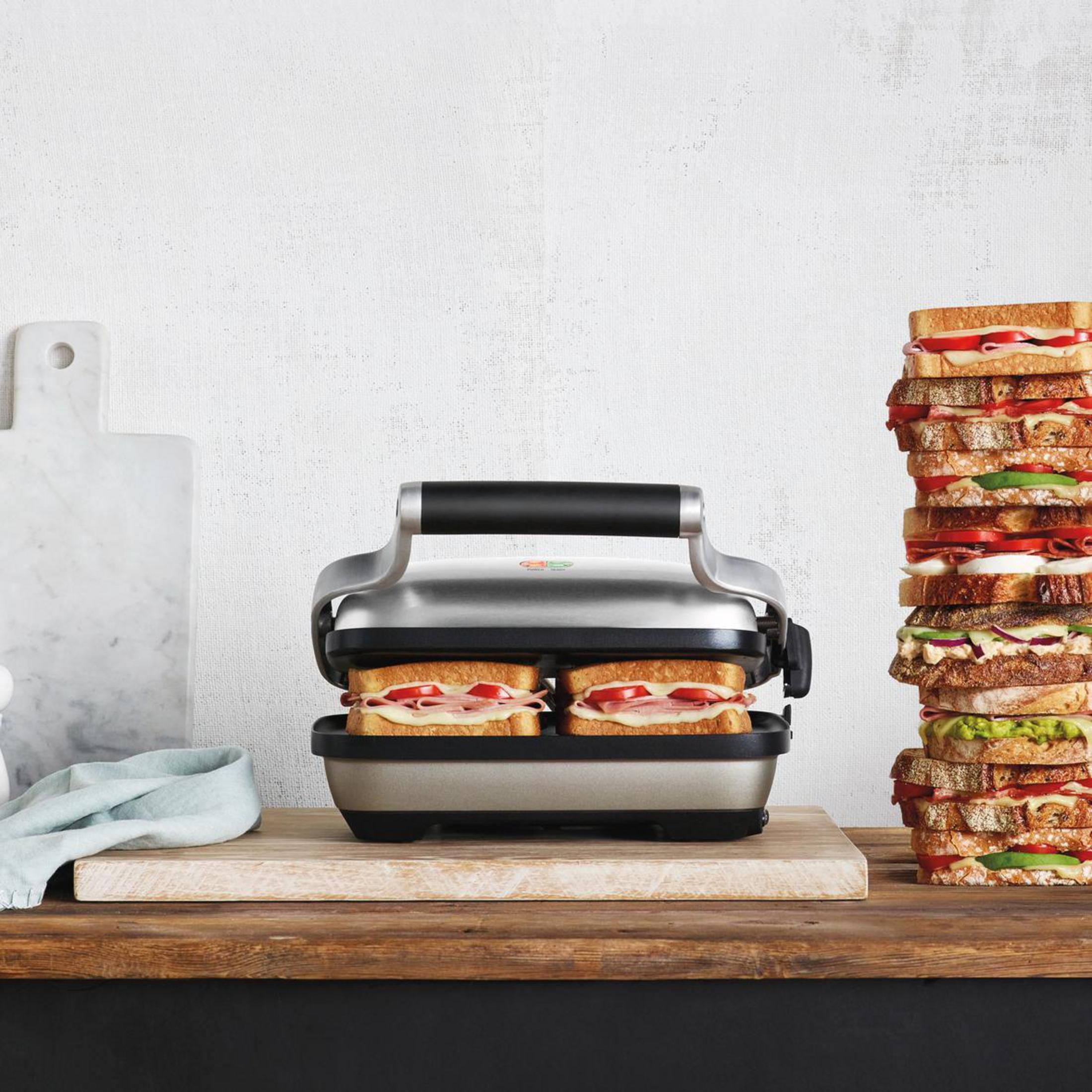 Ein Sandwichmaker mit zwei Sandwiches und einem Stapel Sandwiches rechts.