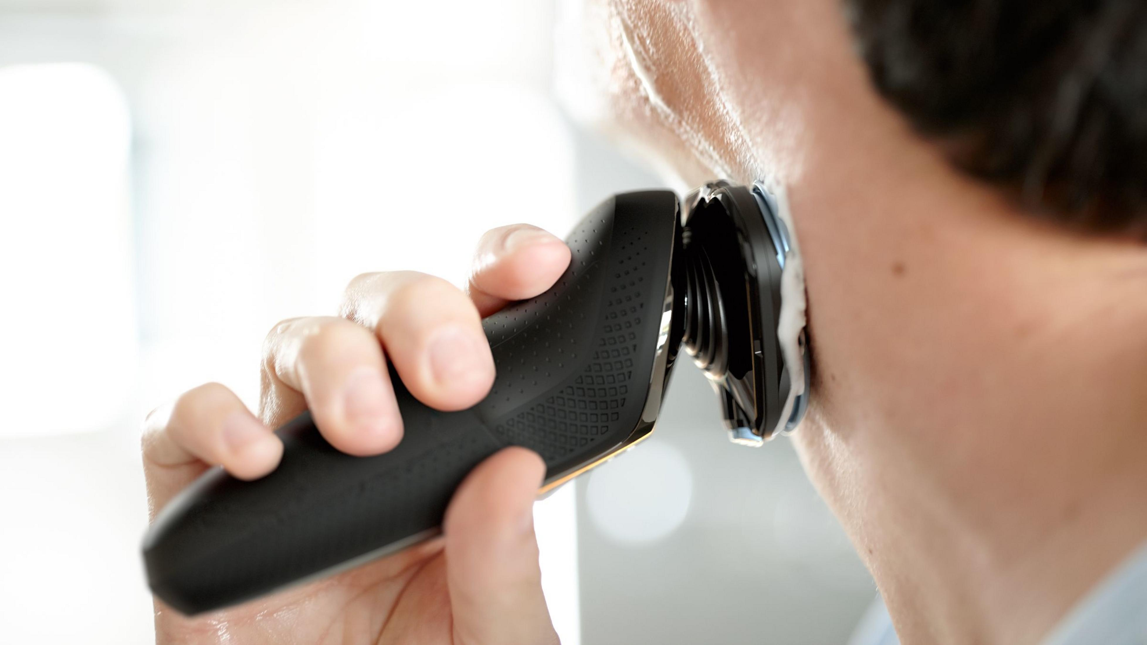 Primo piano di un uomo che si rade il collo con un rasoio elettrico nero.