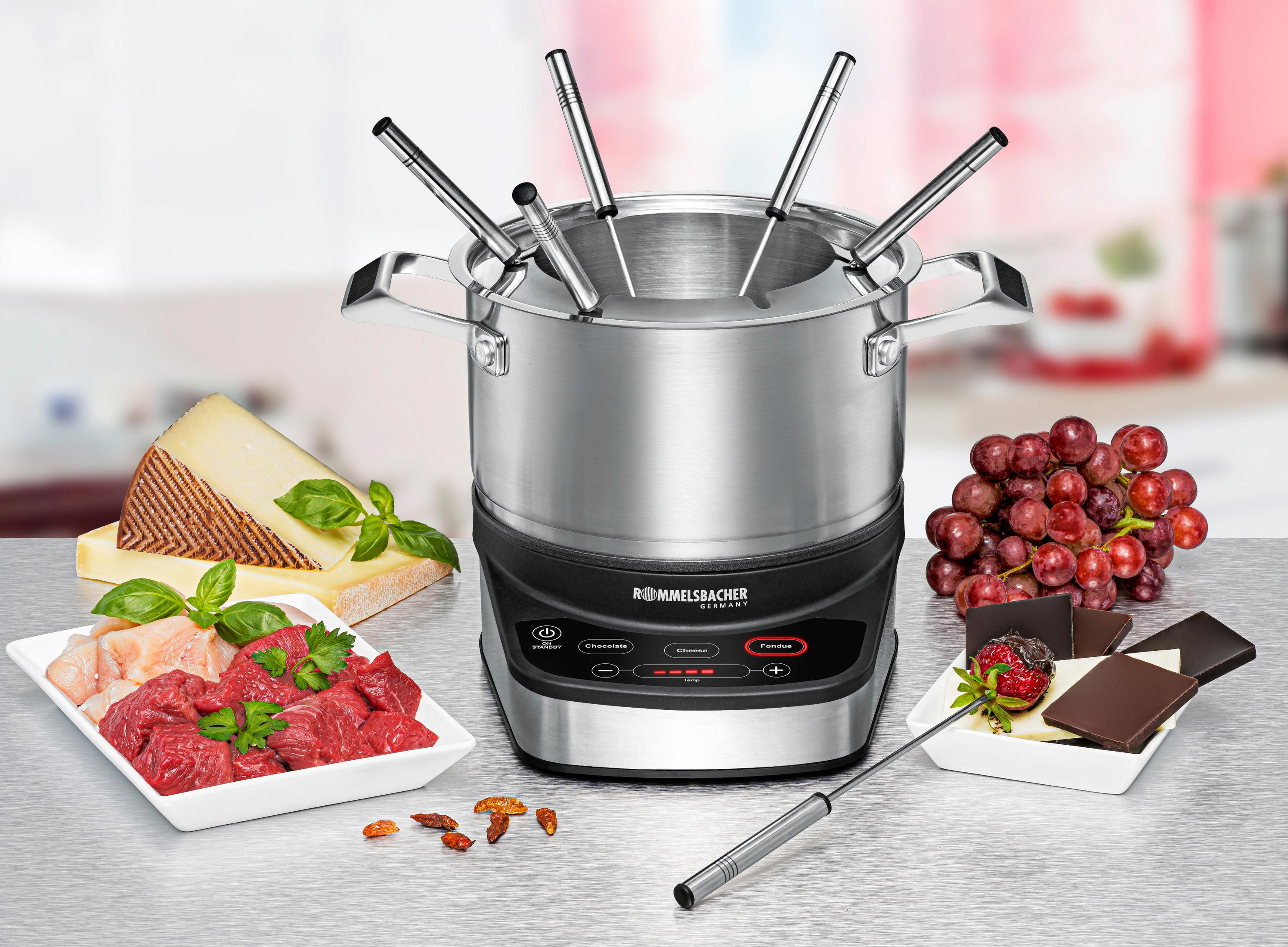 Ein Fondue-Topf mit verschiedenen Lebensmitteln. Enthält Käse, Trauben, Schokolade und rohes Fleisch.