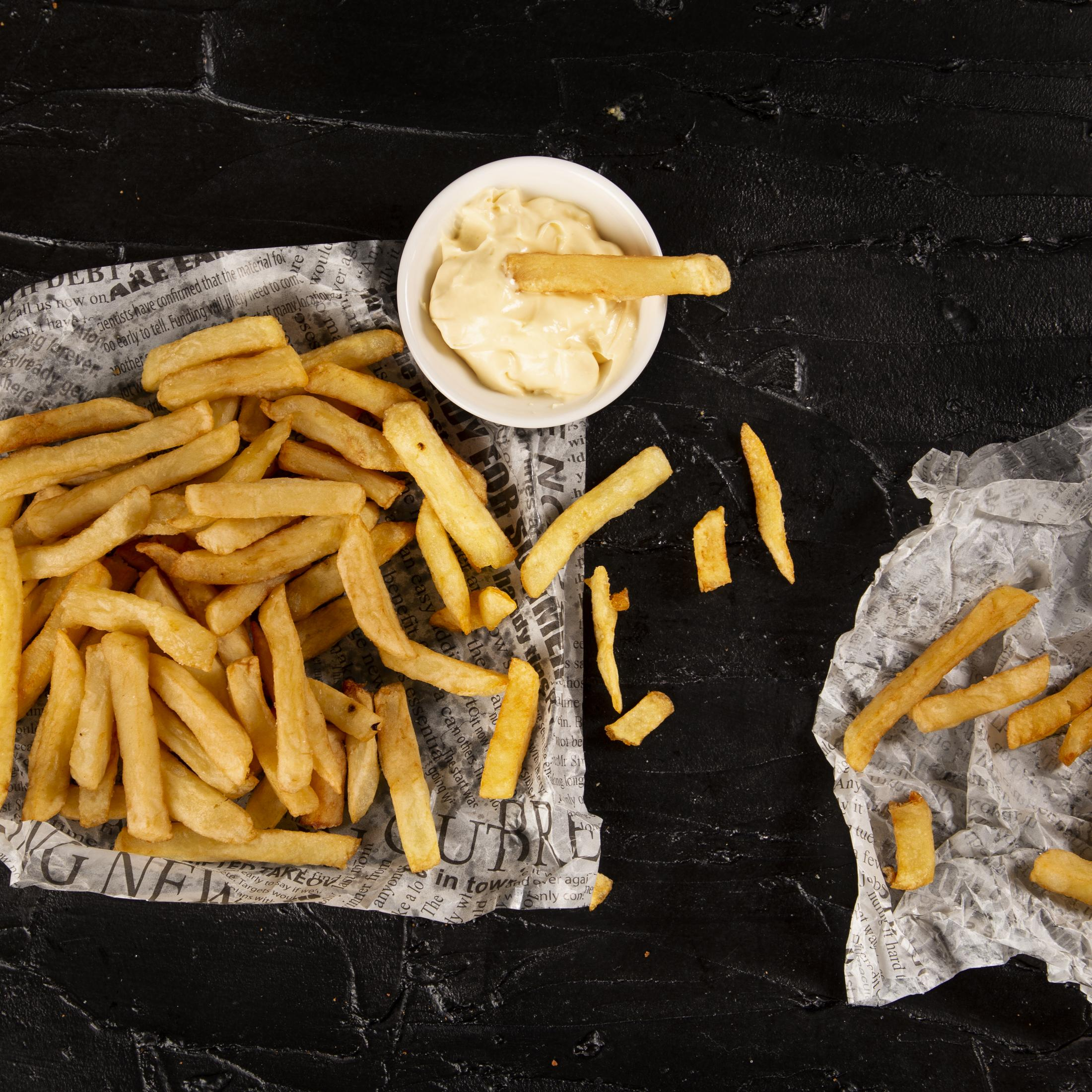 Frytki z majonezem w misce, na gazecie, czarne tło.