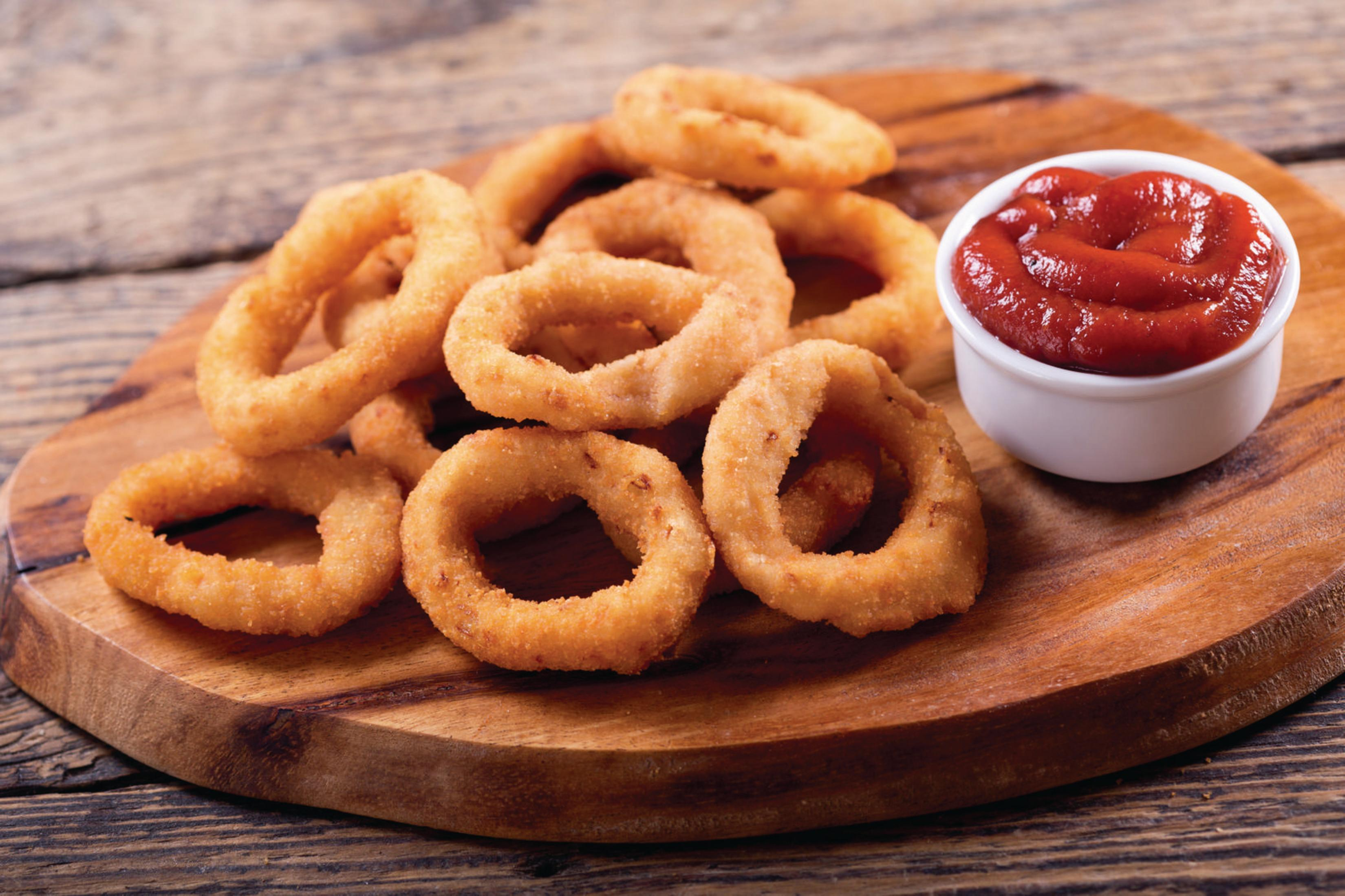Tavola di legno con anelli di cipolla fritti e una piccola ciotola di ketchup su un tavolo di legno.