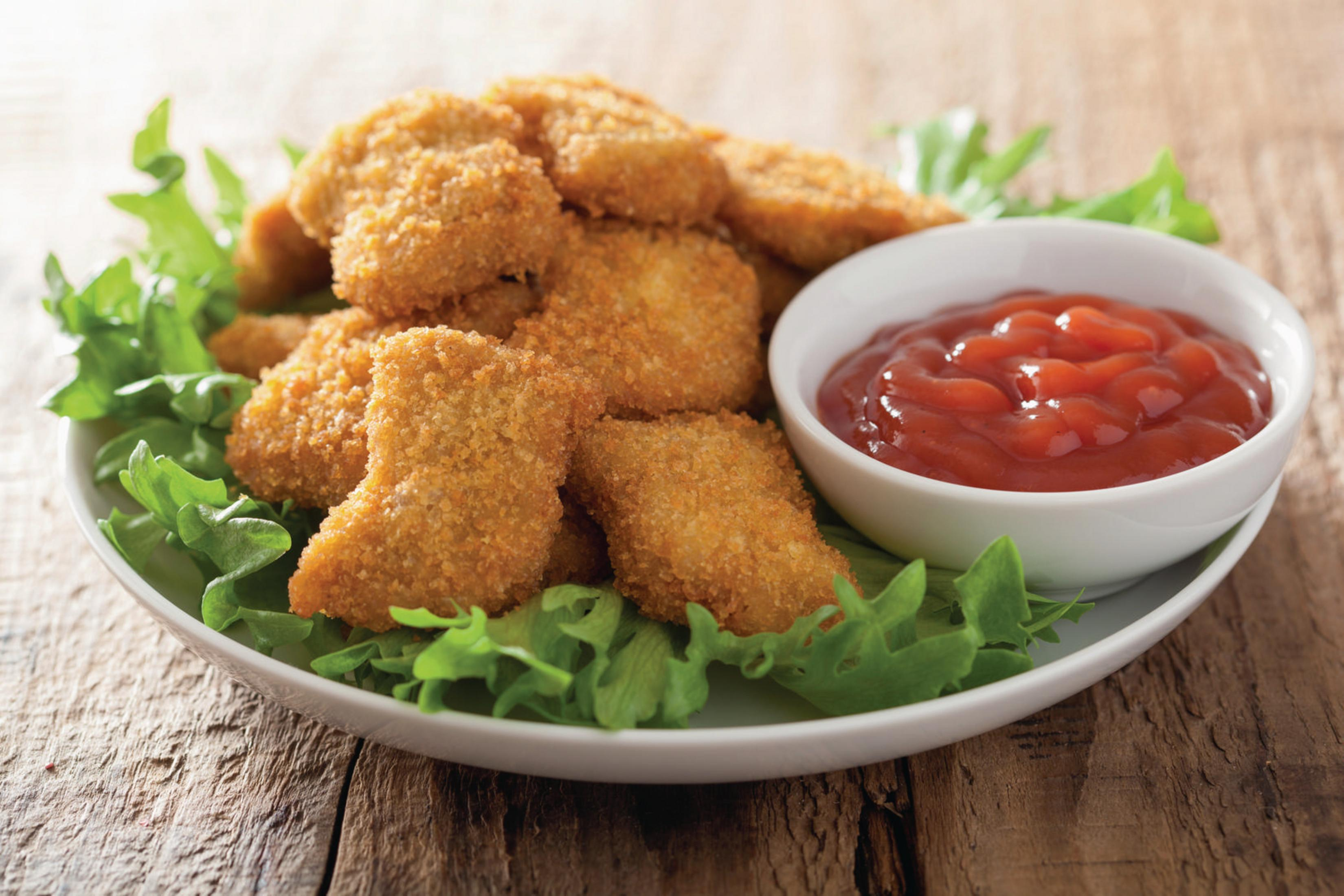 Talerz nuggetów z kurczaka na sałacie, z miską ketchupu na drewnianym stole.