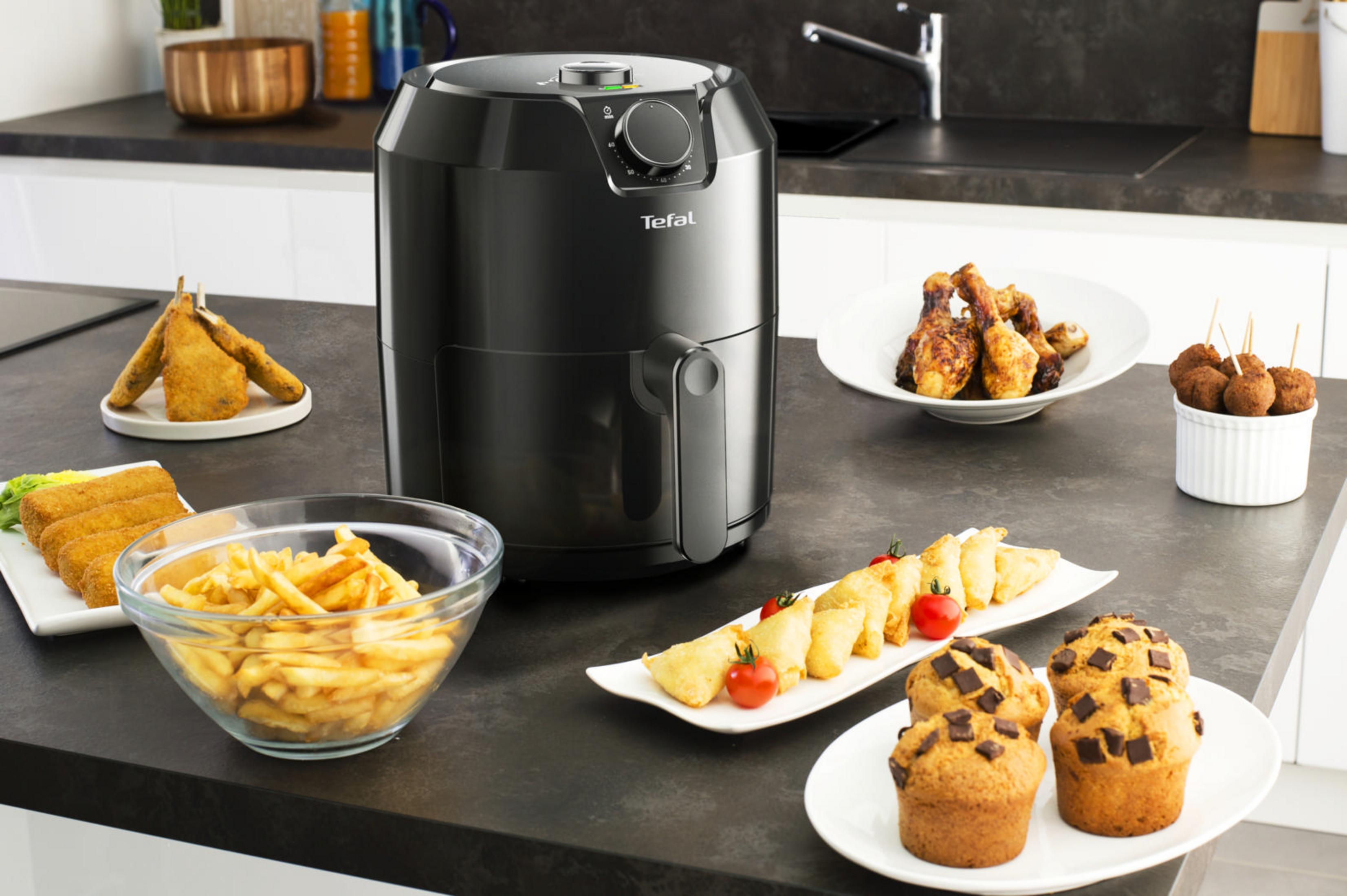 Friggitrice ad aria con cibo sul tavolo, tra cui patatine fritte, pollo e muffin.