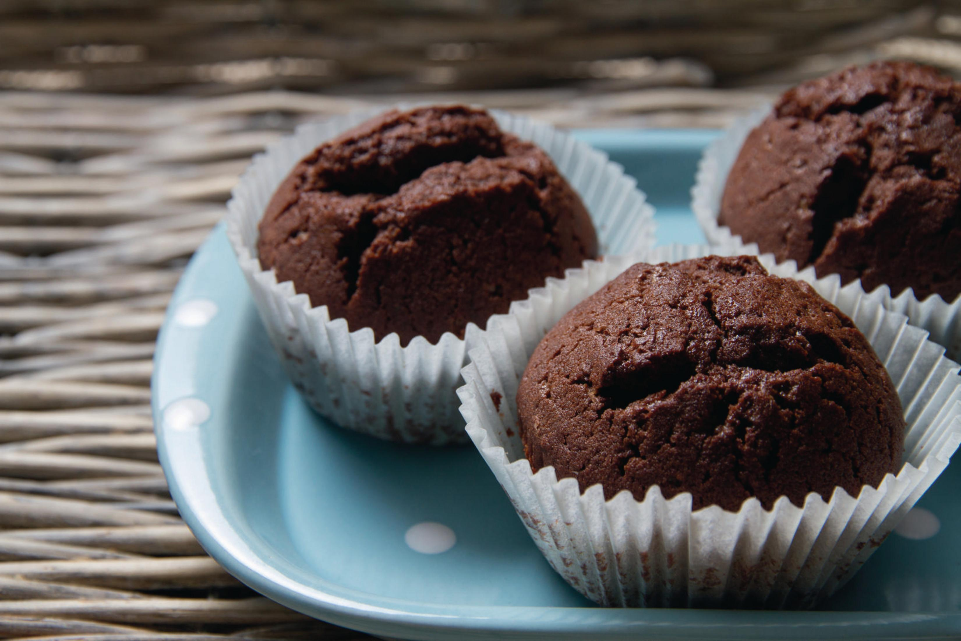 Trzy czekoladowe muffiny w białych papilotkach, na jasnoniebieskim talerzu z białymi kropkami.