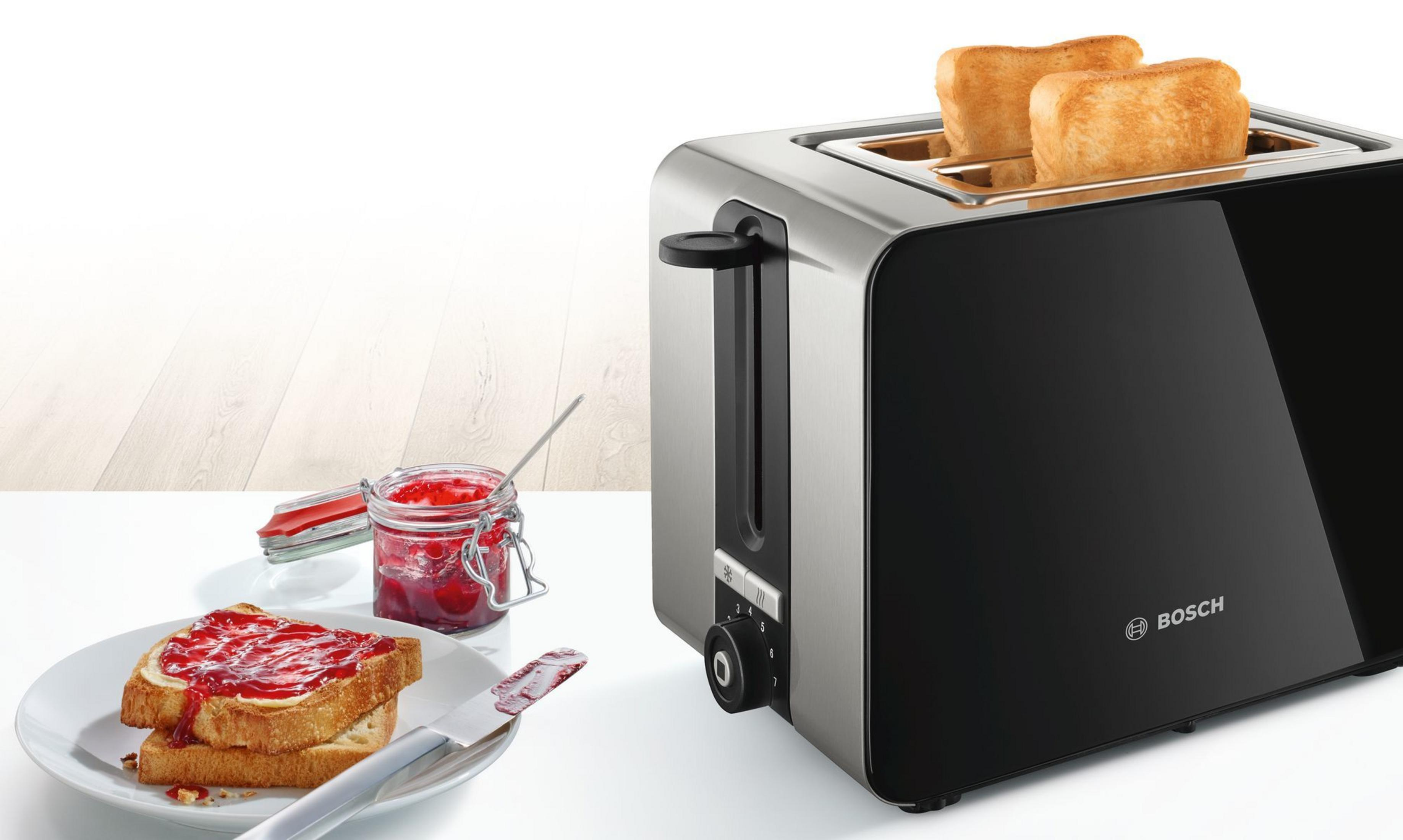 Toaster mit zwei Toastscheiben und Marmelade auf Brot. Ein Marmeladenglas und ein Messer liegen auf dem Tisch.