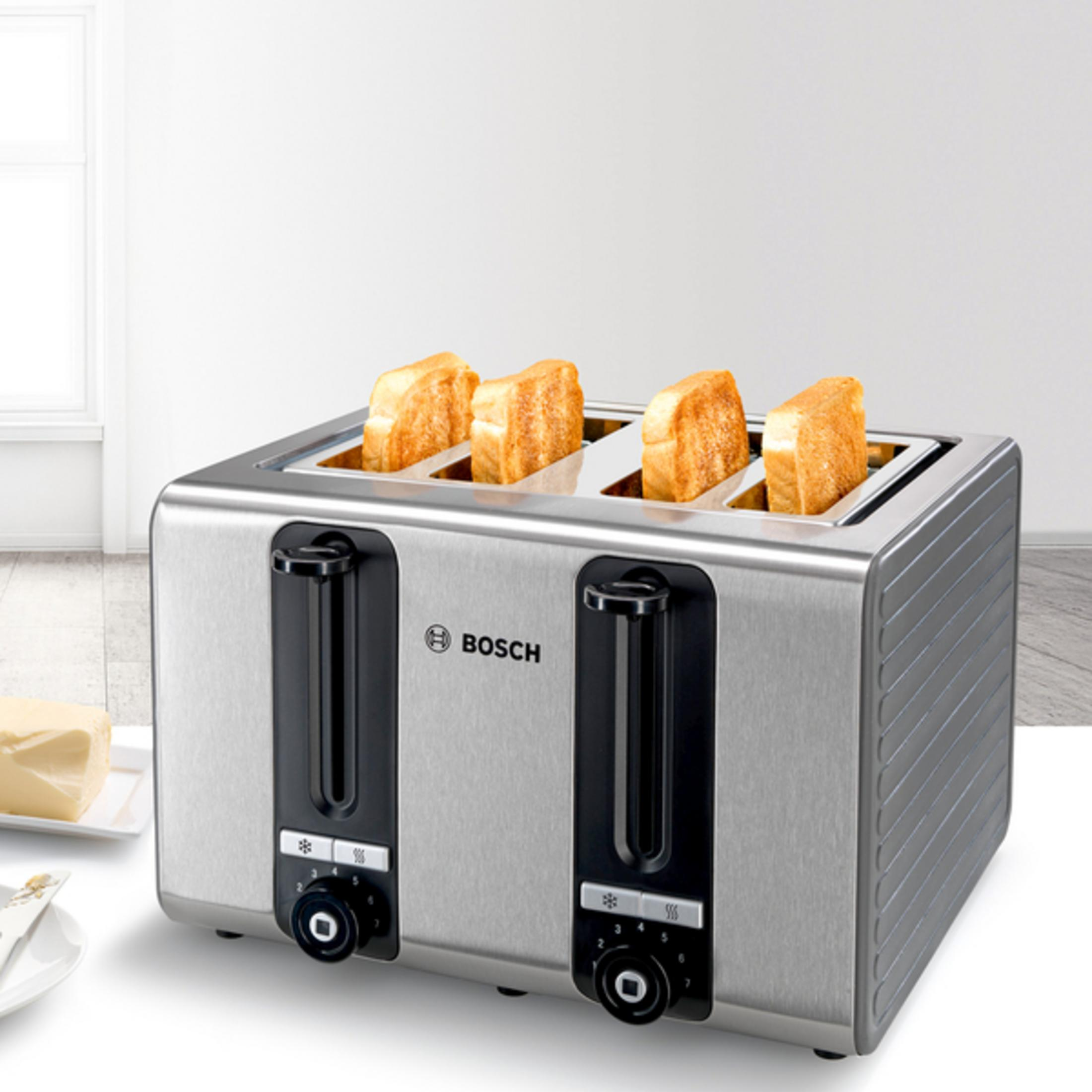 Ein Toaster aus Edelstahl mit vier Toastscheiben und Butter auf einem Teller.
