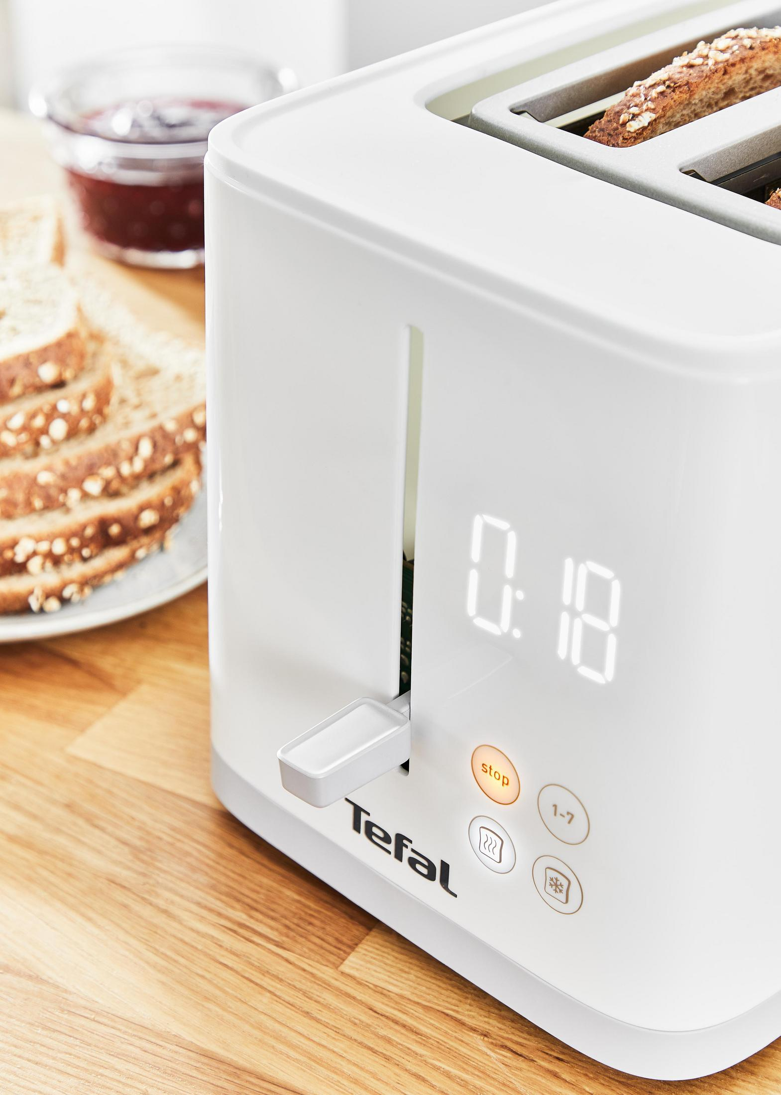 Weißer Toaster mit Brotscheiben, Marmeladenglas und Holztisch.