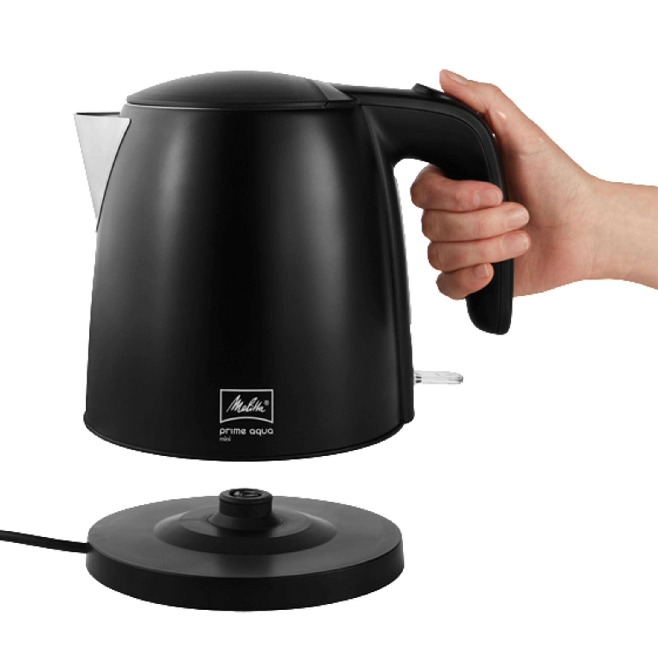 Een zwarte waterkoker met een hand die de handgreep vasthoudt. De waterkoker staat op zijn voet, geïsoleerd.