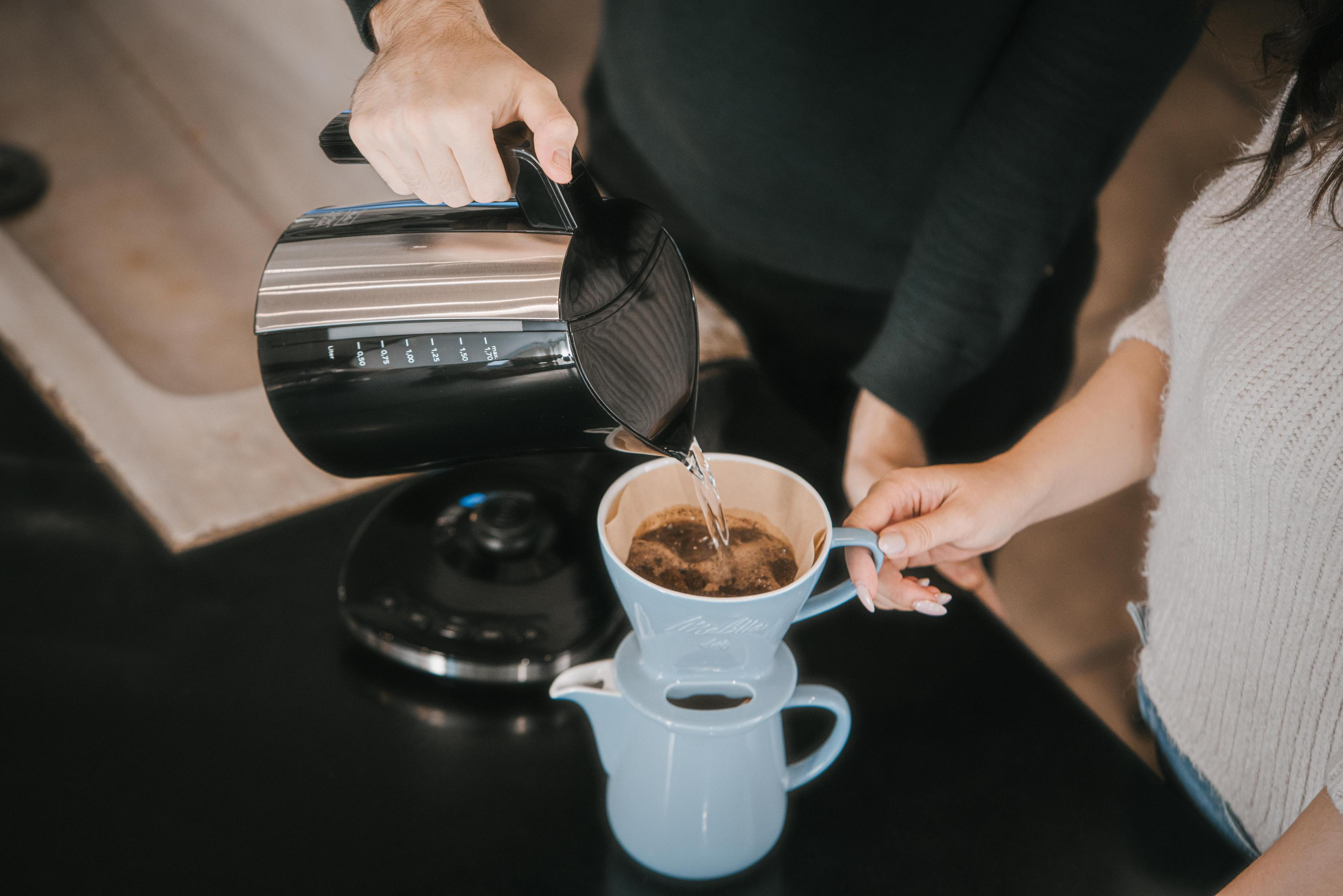 Osoba wlewa gorącą wodę z czajnika do filtra z fusami kawy.