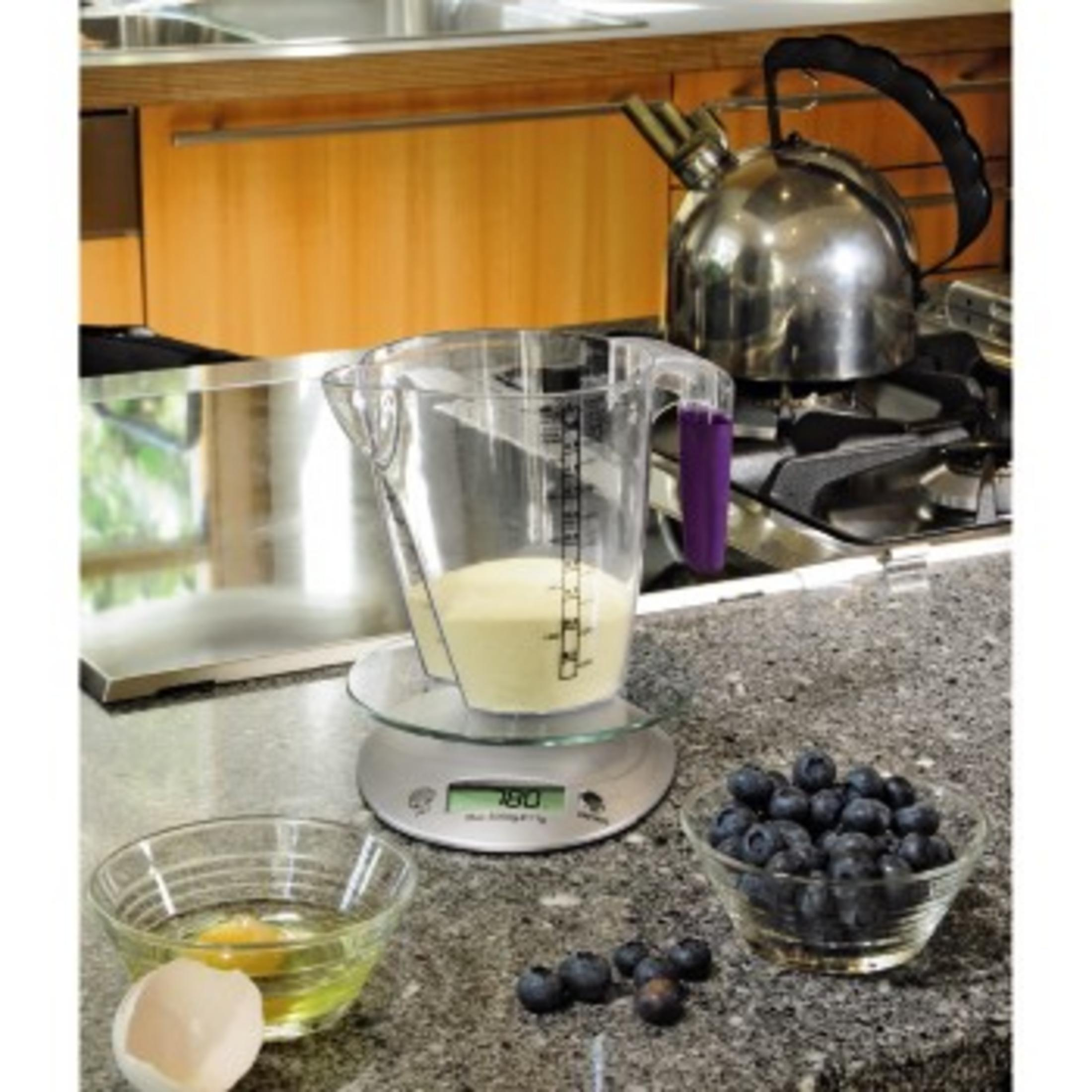 Dzbanek z miarką na wadze, miska z jagodami, miska z jajkiem. Otoczenie kuchenne.