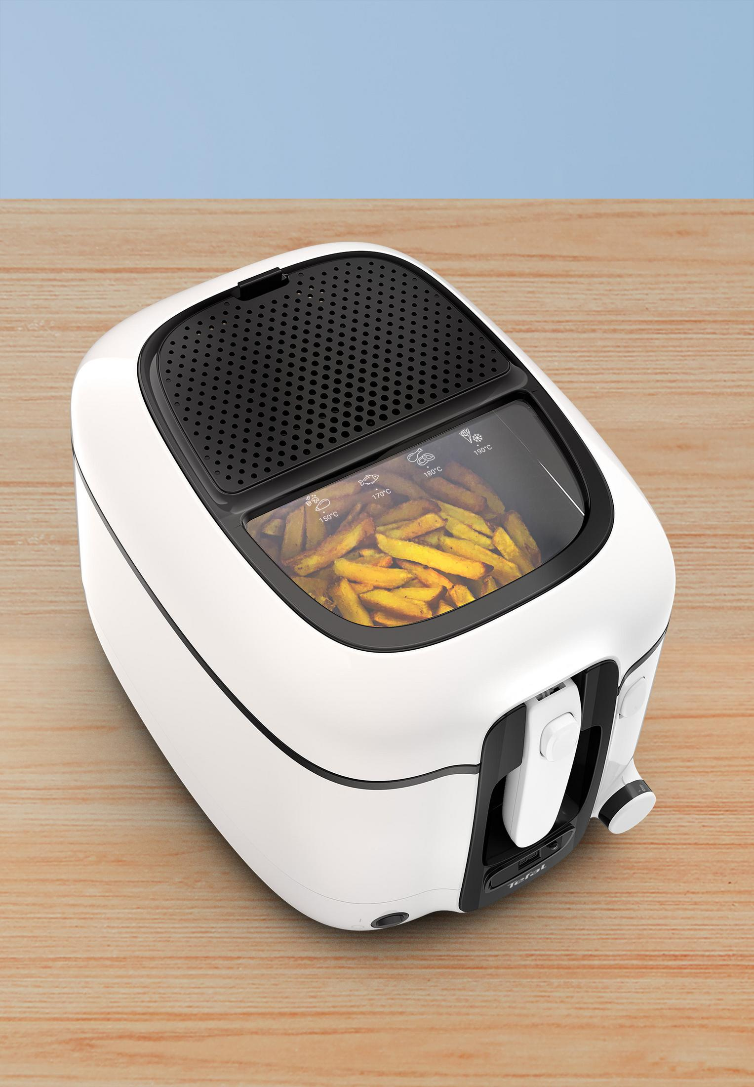 Biała frytkownica z frytkami w środku. Tło to drewniany stół i niebieska ściana.