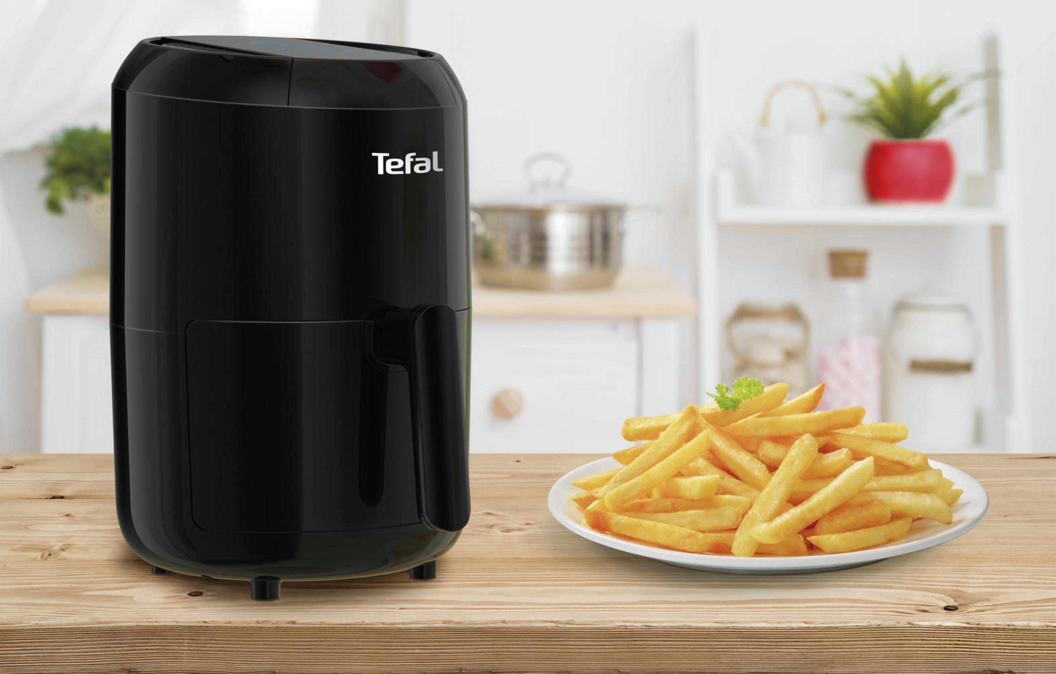 Schwarze Heißluftfritteuse mit Pommes auf einem Teller, auf einem Holztisch, Küchenhintergrund.