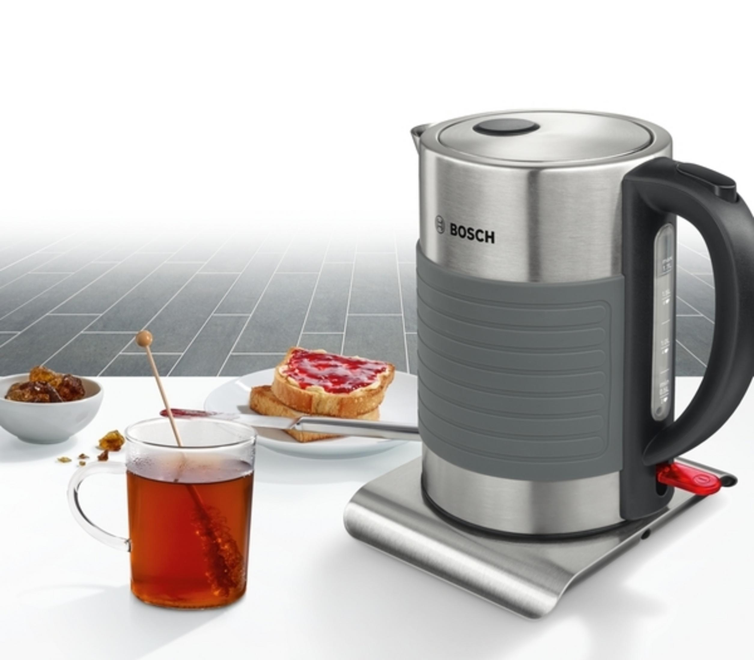 Edelstahlkessel mit schwarzem Griff und eine Tasse Tee mit Toast und Marmelade.