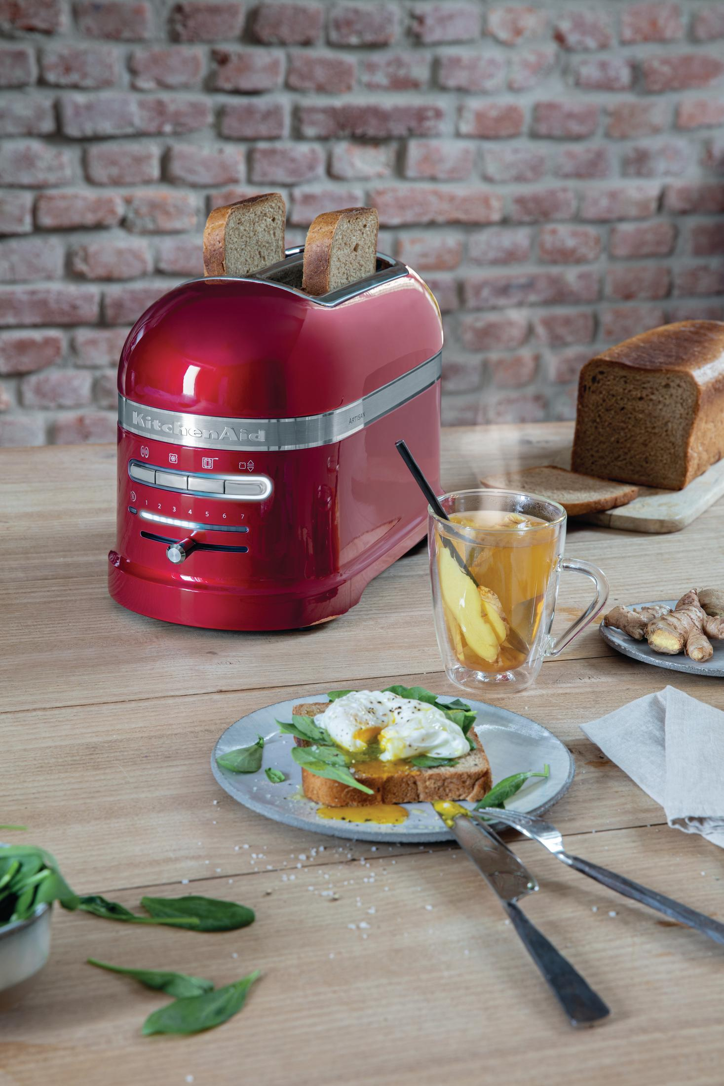 Roter KitchenAid Toaster mit zwei Toastscheiben. Ein Glas Tee und ein Teller mit pochiertem Ei sind sichtbar.