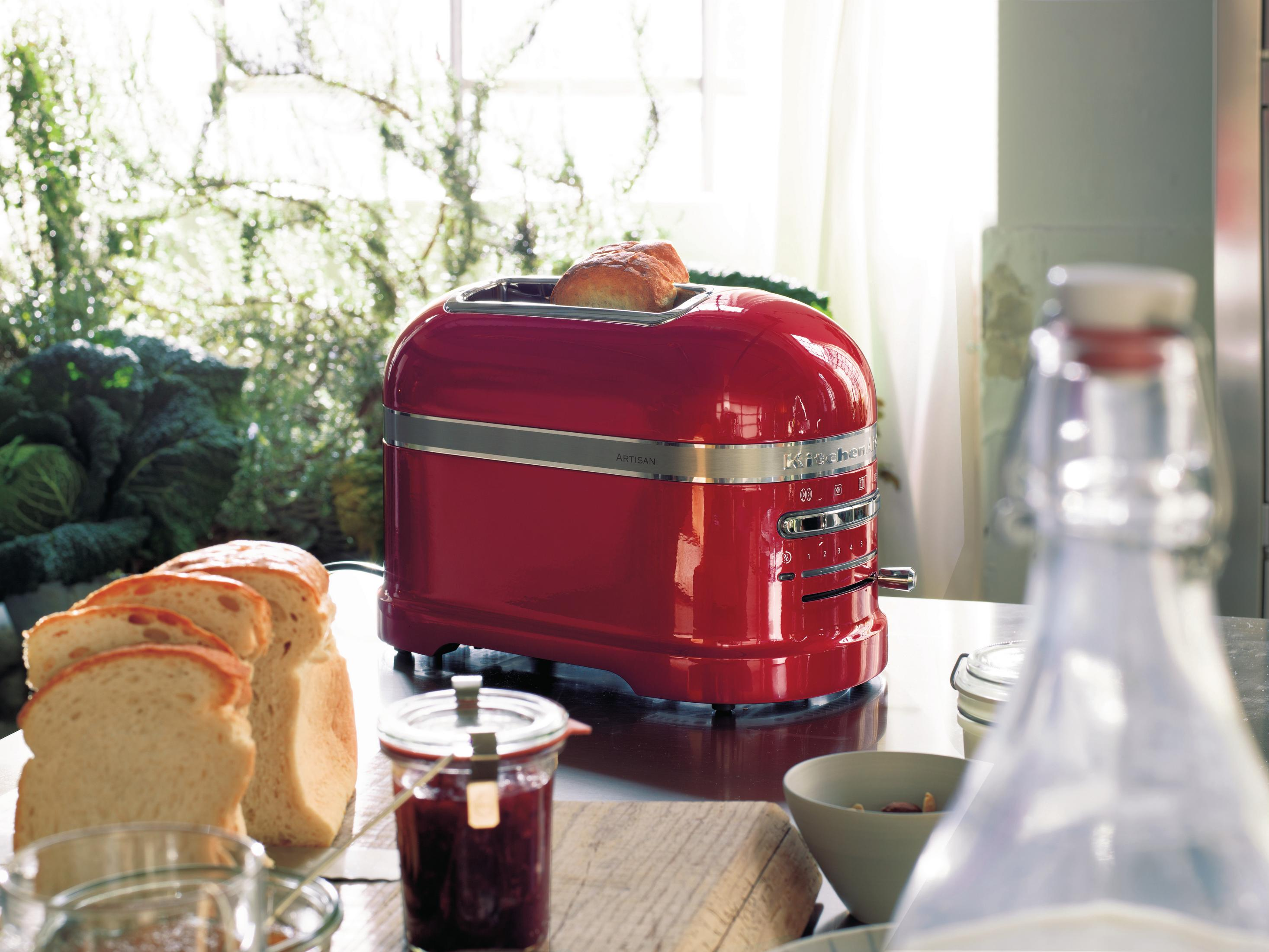Ein roter KitchenAid Toaster mit Brot und Marmelade auf Holzoberfläche.