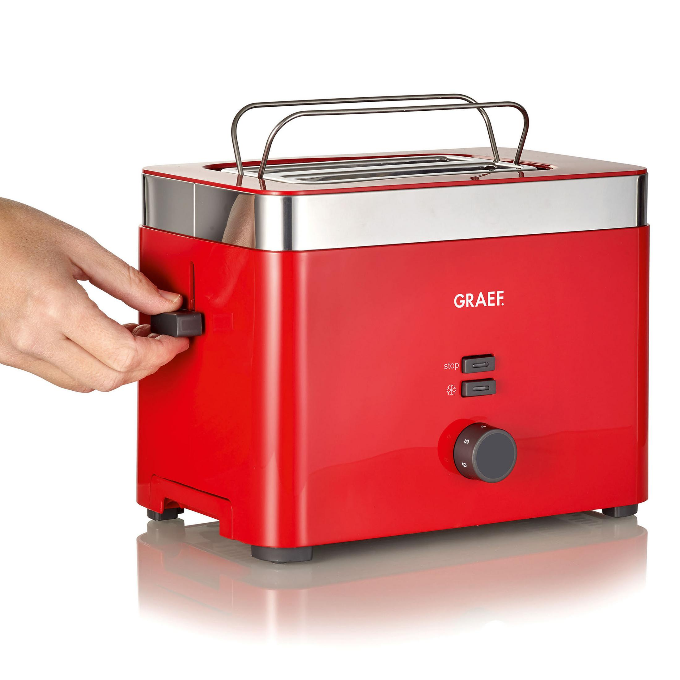 Roter Toaster mit silbernem Griff und Bedienelementen. Eine Hand stellt den Bräunungsgrad ein.