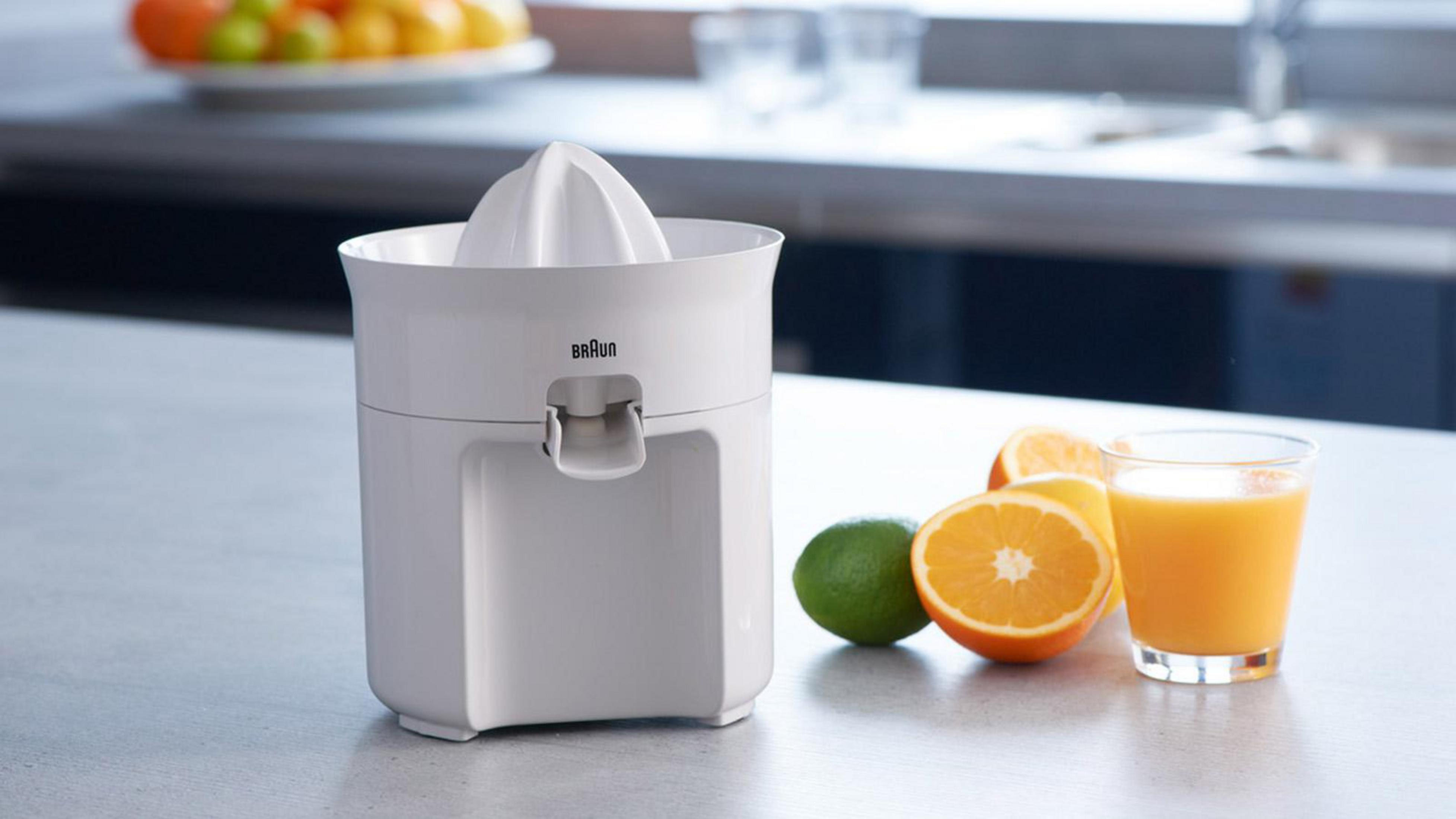 Una centrifuga bianca con arance, un lime e un bicchiere di succo su un piano chiaro.