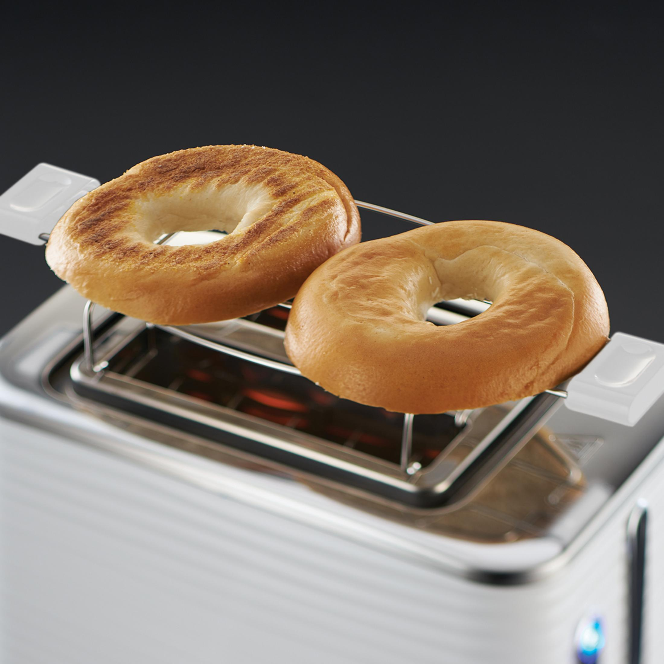 Dos bagels tostados están en una tostadora. La tostadora es blanca con interior de acero inoxidable.