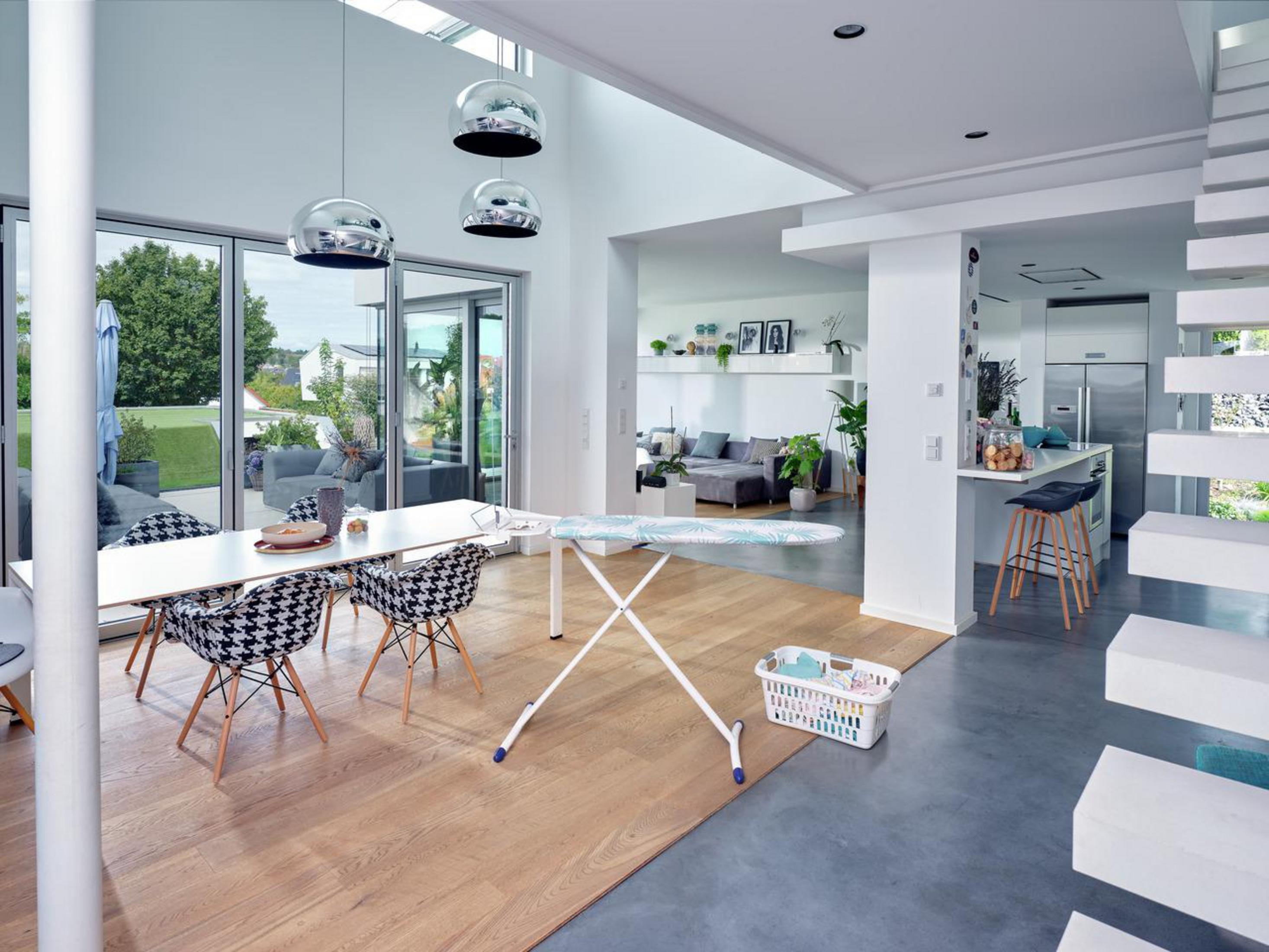 Interior moderno con mesa, sillas, tabla de planchar y cocina abierta.