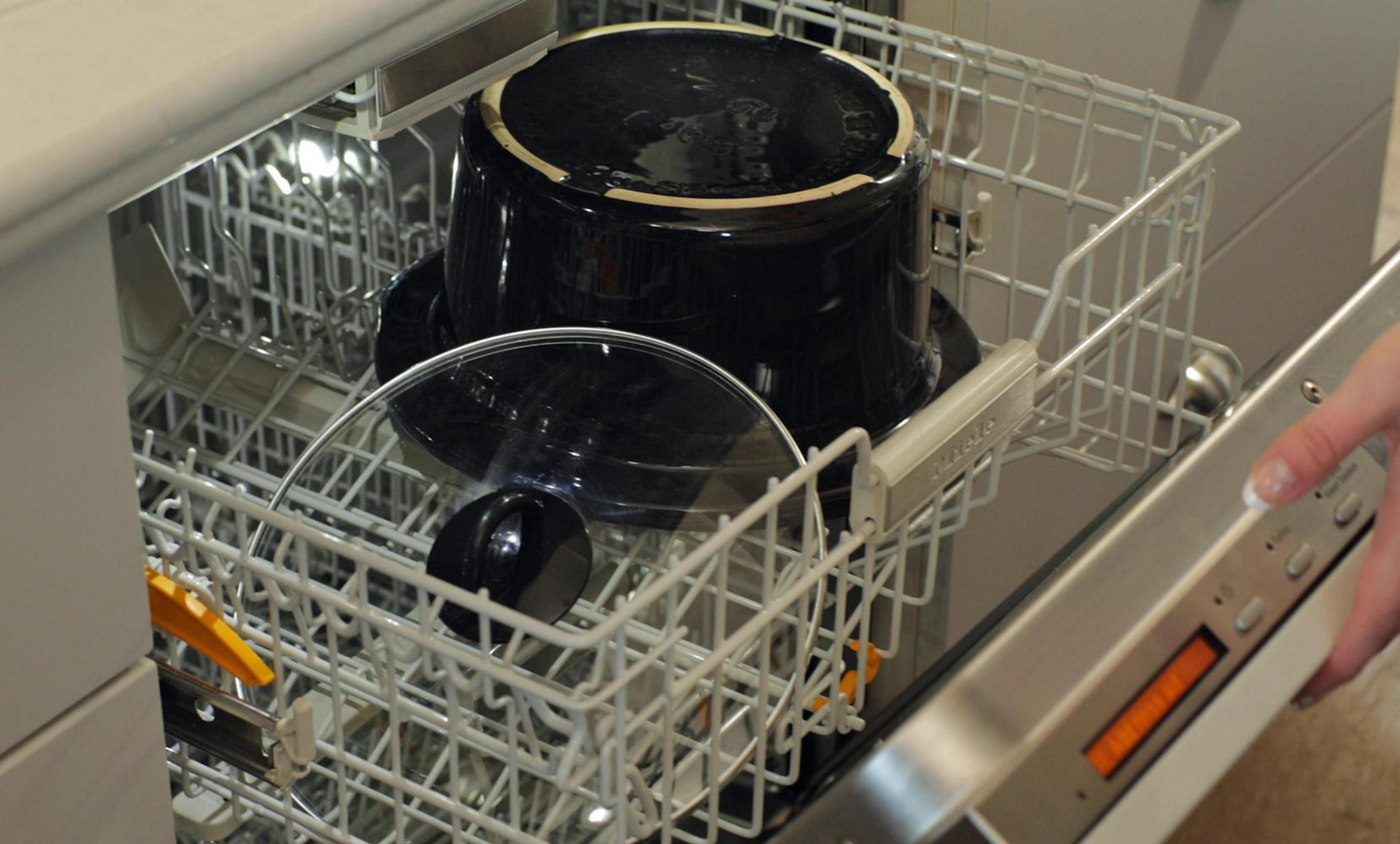 Zmywarka z czarnym garnkiem i szklaną pokrywką w środku. Ręka dotyka panelu sterowania.