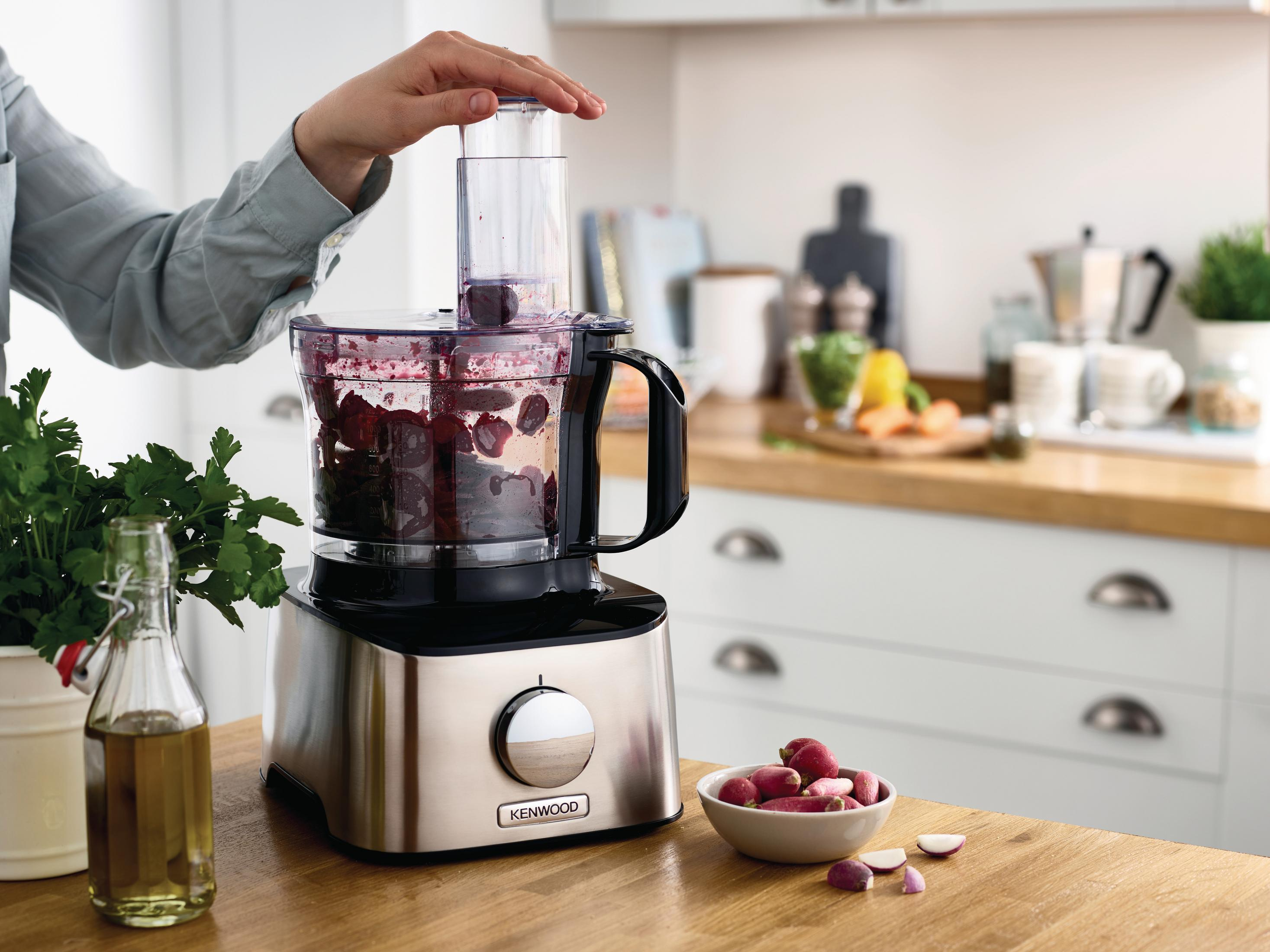 A person's hand is adding cherries to a food processor on a wooden table.