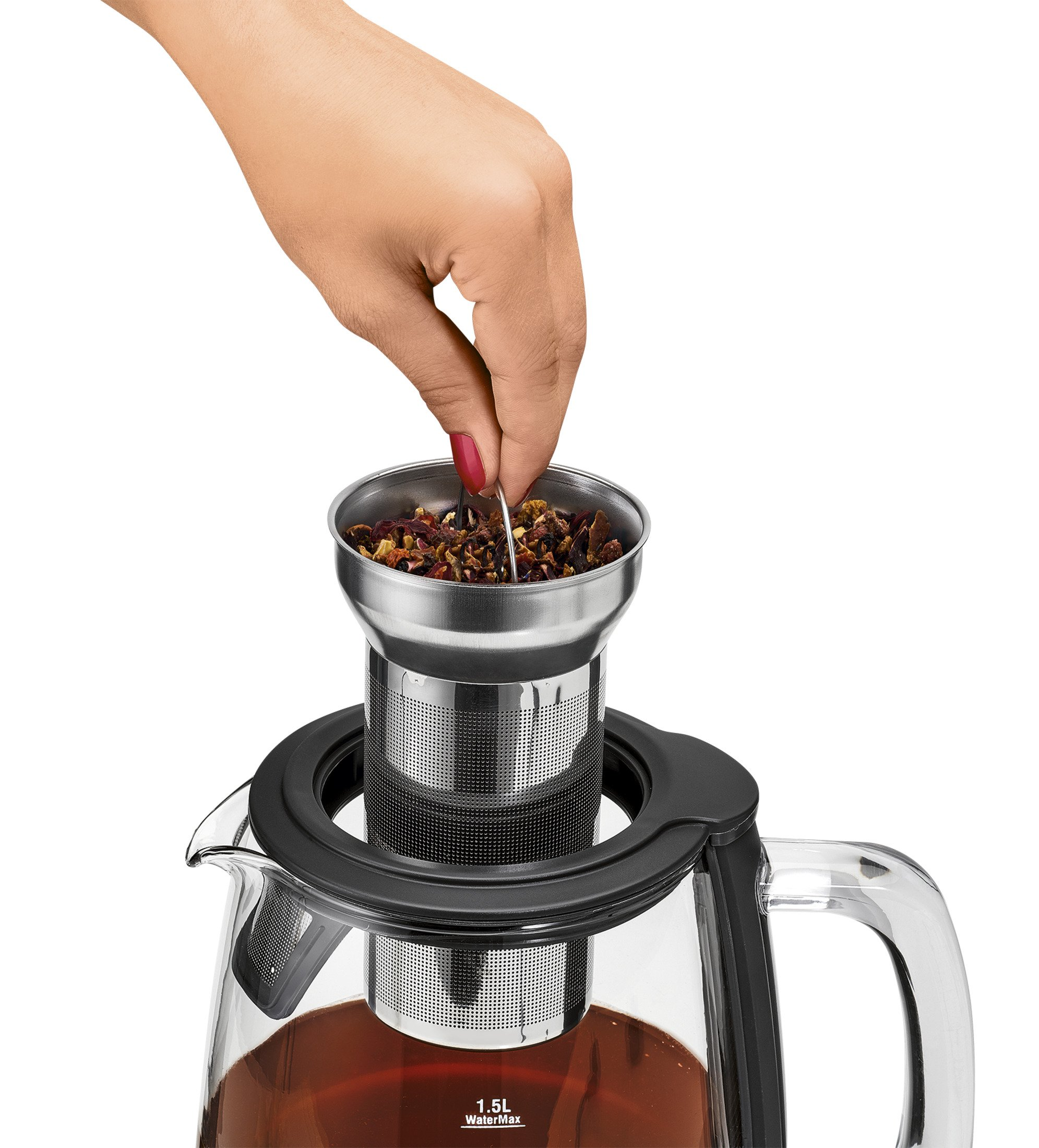 Ręka dodająca liście herbaty do zaparzacza do herbaty w szklanym czajniczku z herbatą.