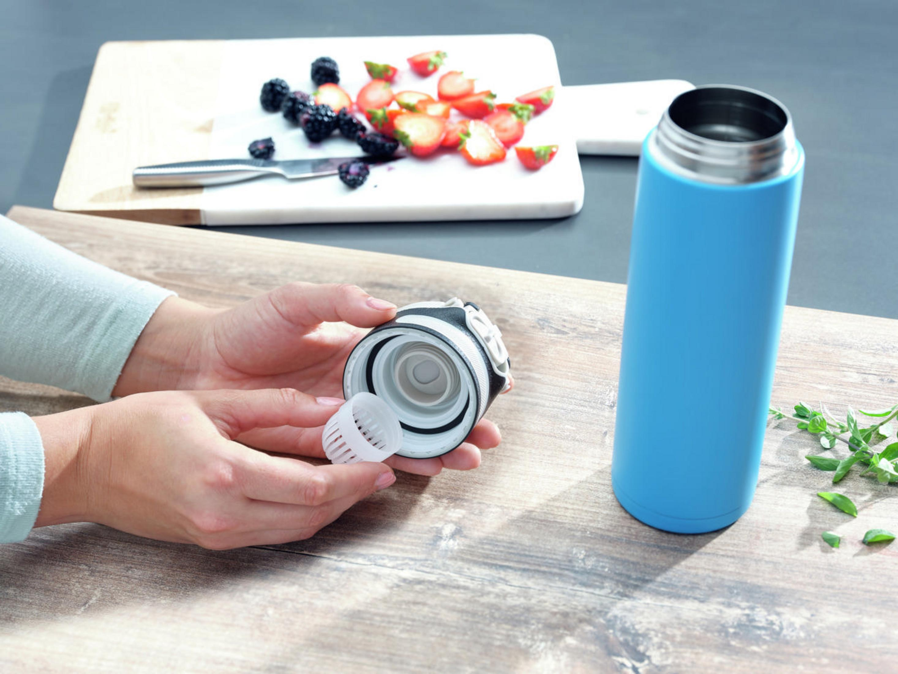 Hände montieren eine blaue Wasserflasche mit Obst, auf Holz.