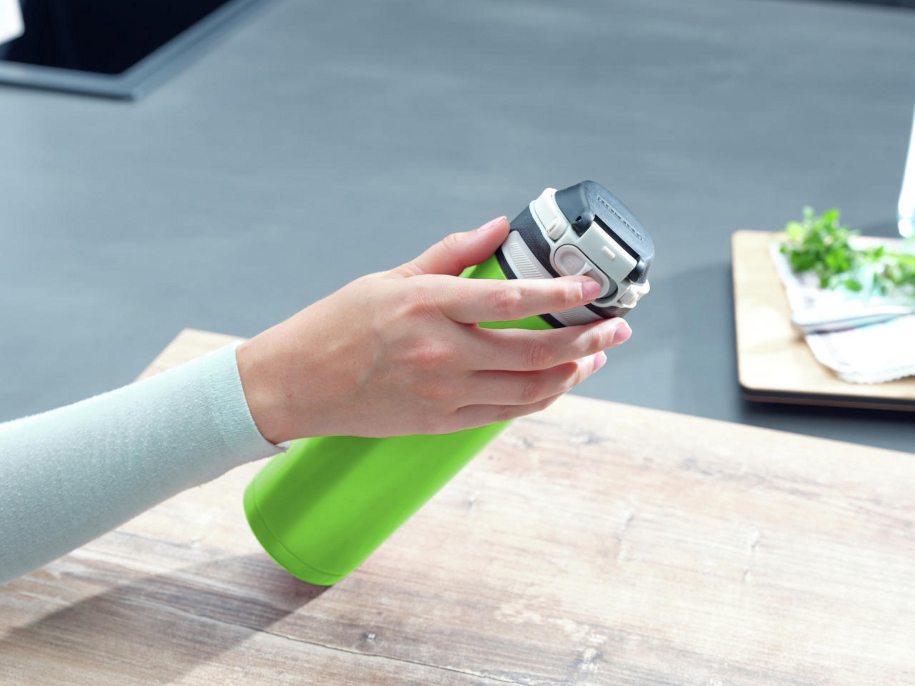 Eine grüne Wasserflasche wird von einer Hand auf einer Holzoberfläche gehalten.