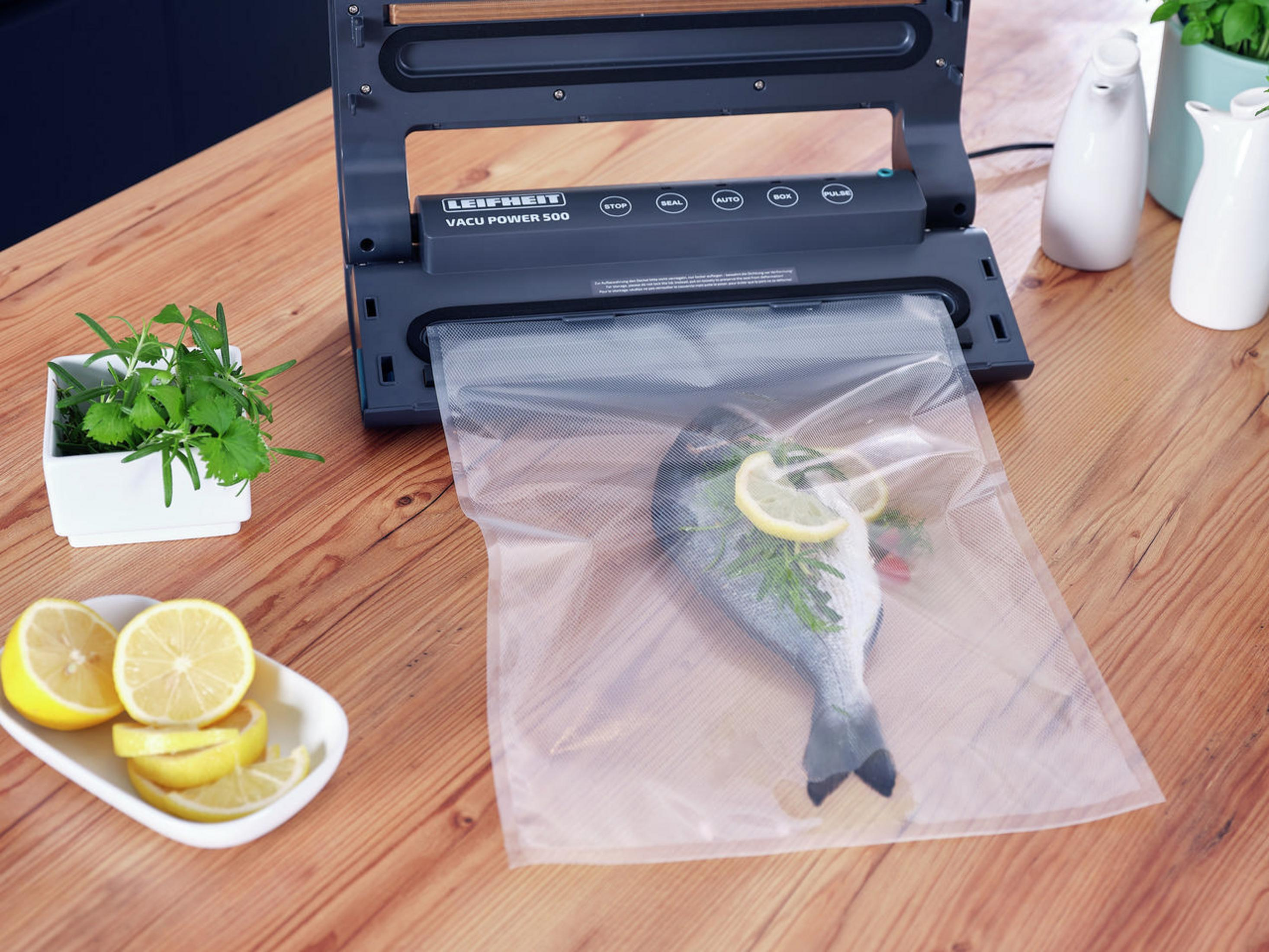 Vakuumiergerät mit Fisch, Zitrone und Kräutern auf Holztisch.