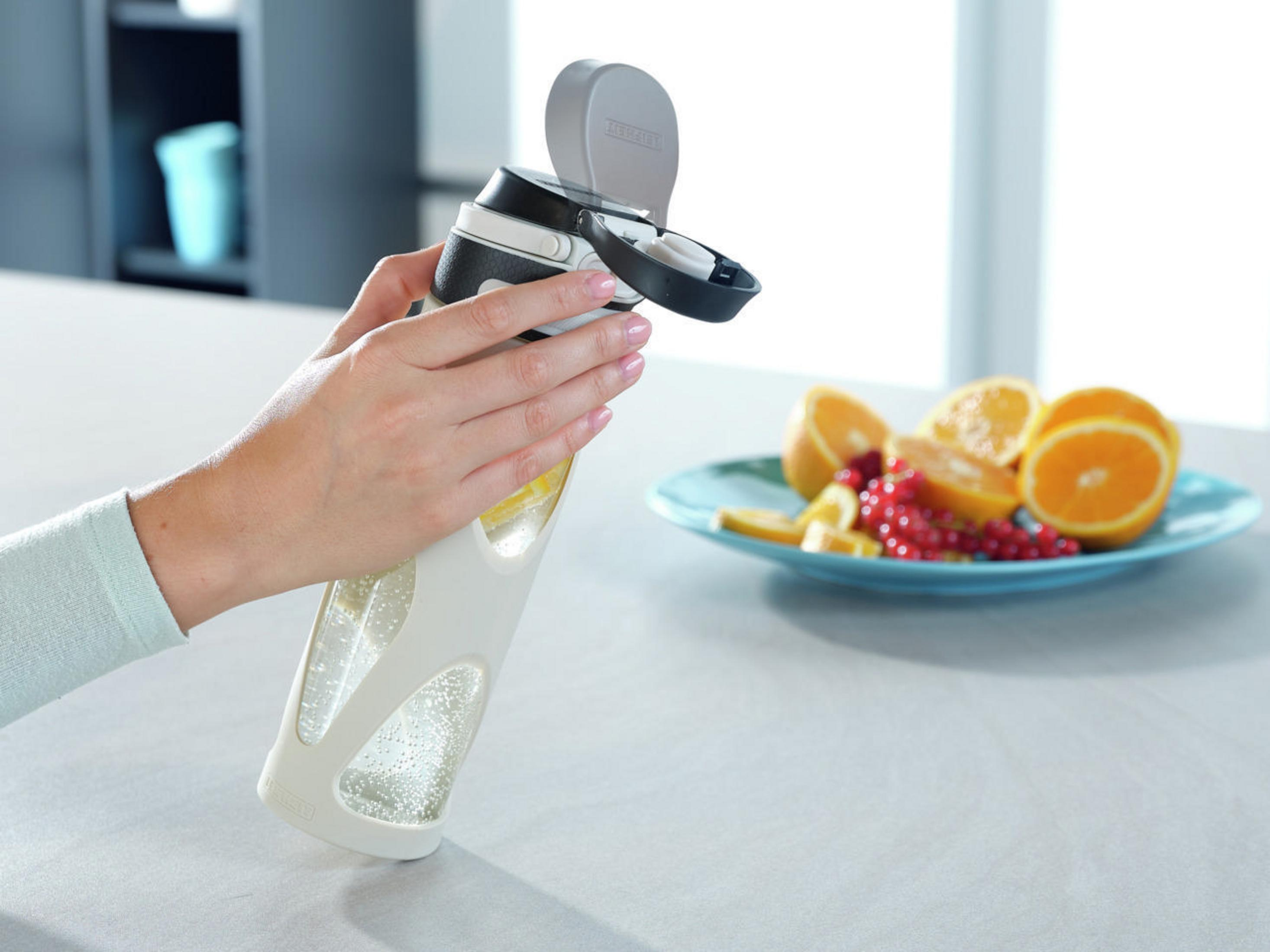 Eine Person öffnet eine Flasche mit Obst. Orangen und Beeren liegen auf einem Teller.