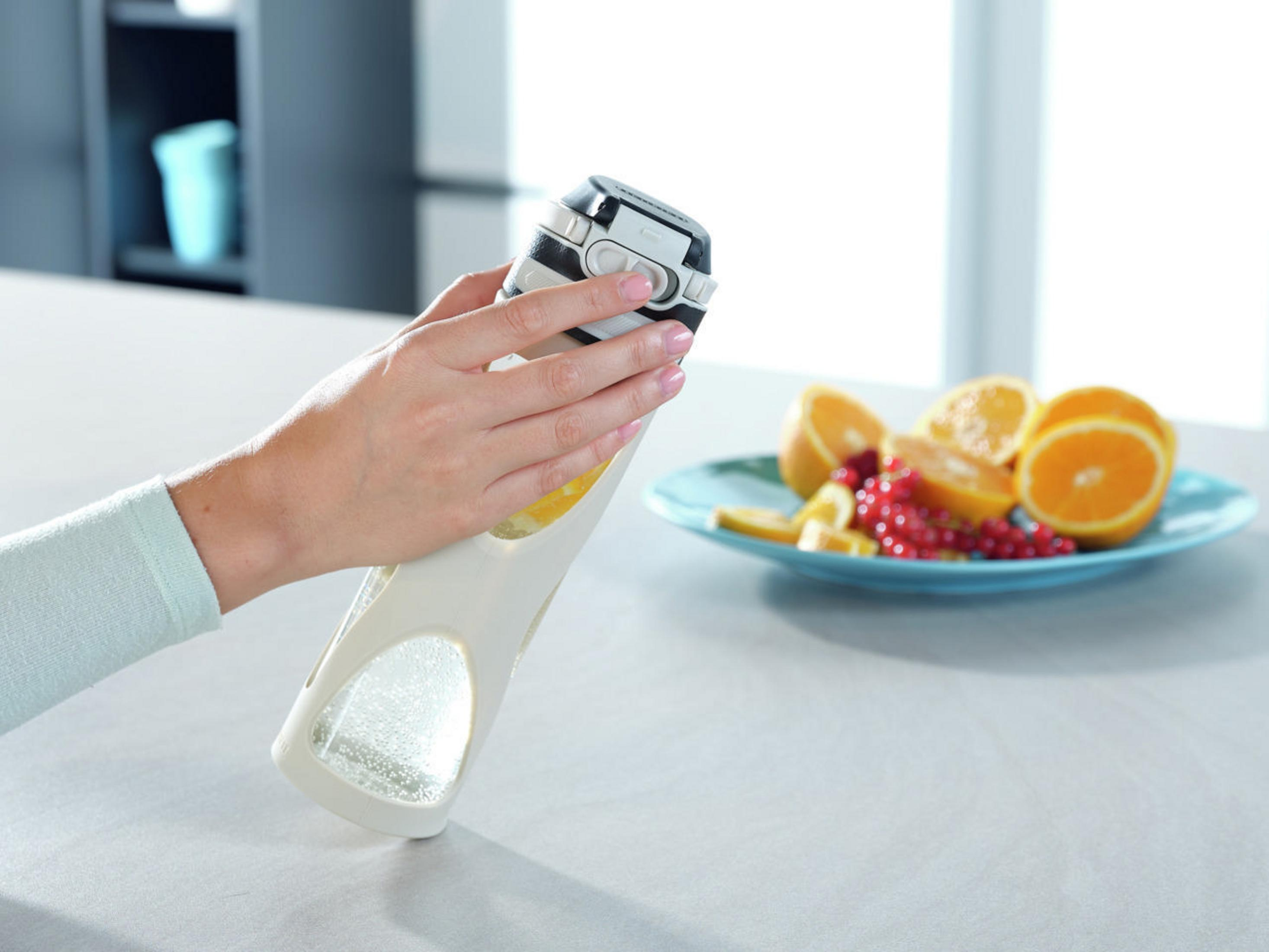 Eine Person hält eine Wasserflasche mit Obst, in der Nähe eines Tellers mit geschnittenem Obst und einer Theke.