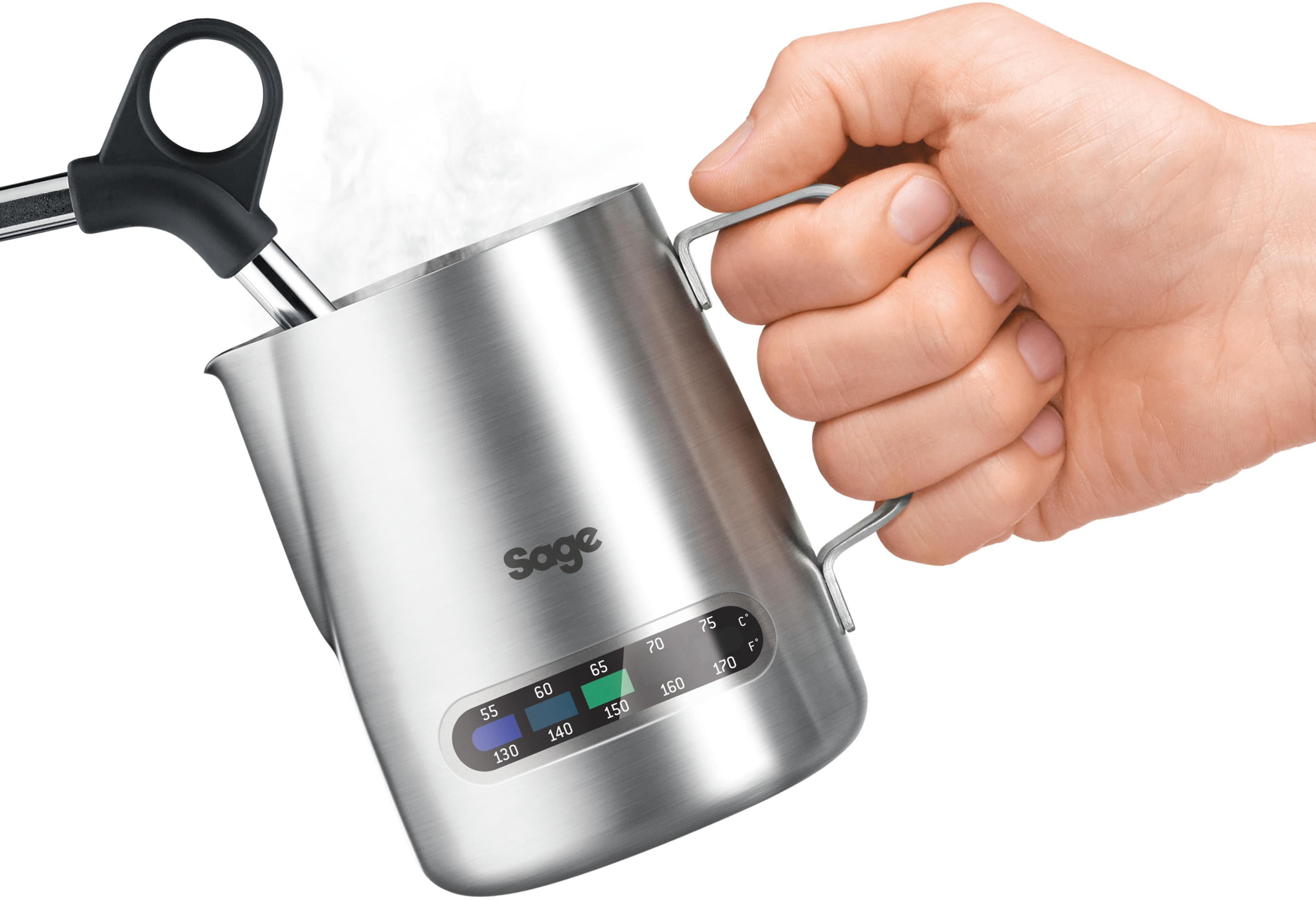 A person holding a silver milk frothing pitcher, with a thermometer, and a steam wand.