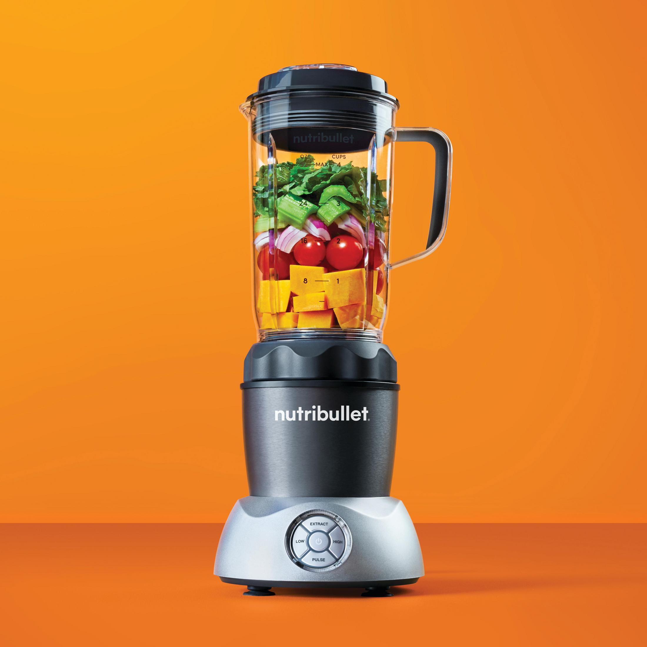 Un frullatore Nutribullet pieno di verdure e frutta, su uno sfondo arancione.