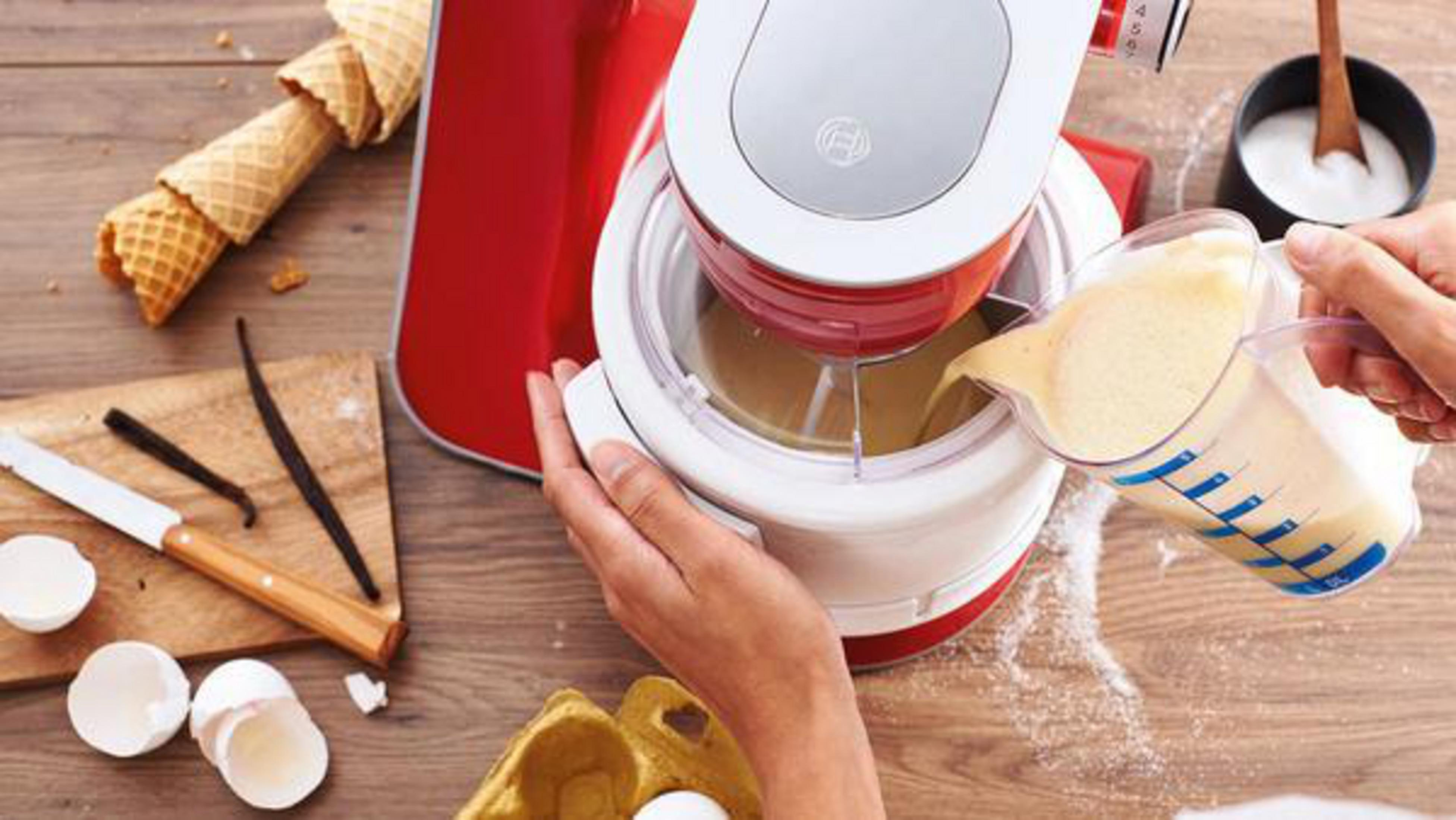 Czerwono-biała maszyna do lodów w użyciu, składniki jak jajka i wanilia na drewnianym stole.