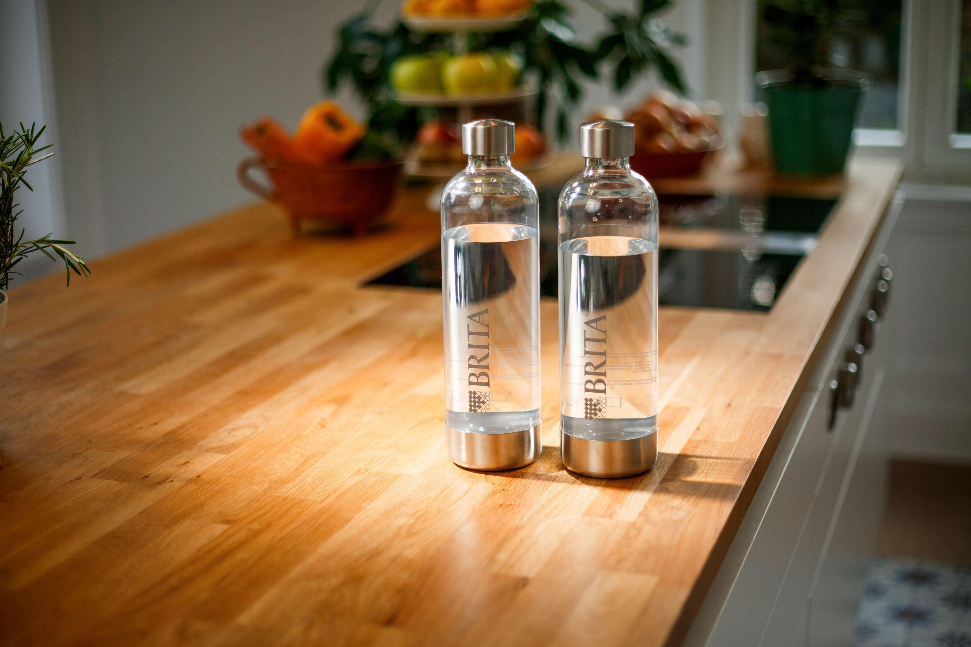 Zwei Glaswasserflaschen mit der Aufschrift 'BRITA' auf einer hölzernen Arbeitsplatte, mit Küchenhintergrund.