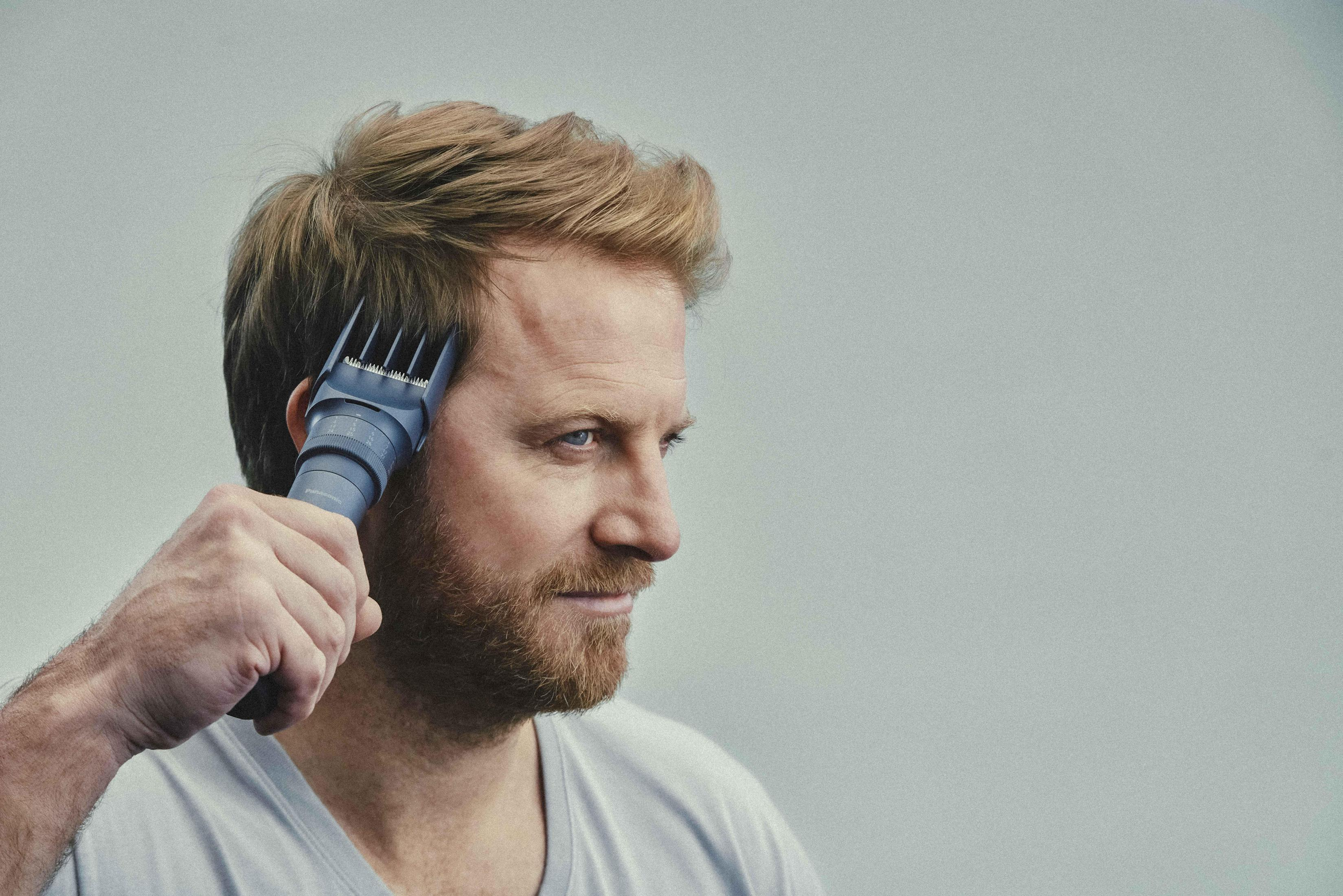 Ein Mann benutzt einen Haarschneider, um sich die Haare zu schneiden. Grauer Hintergrund.