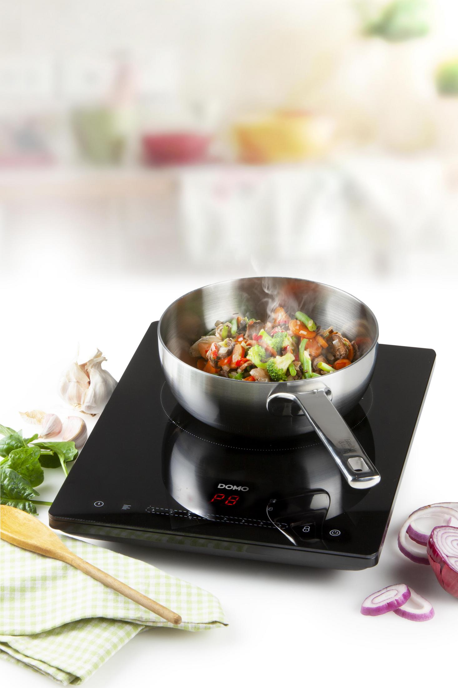 Patelnia z gotowanymi warzywami na płycie indukcyjnej z cyfrowym wyświetlaczem.