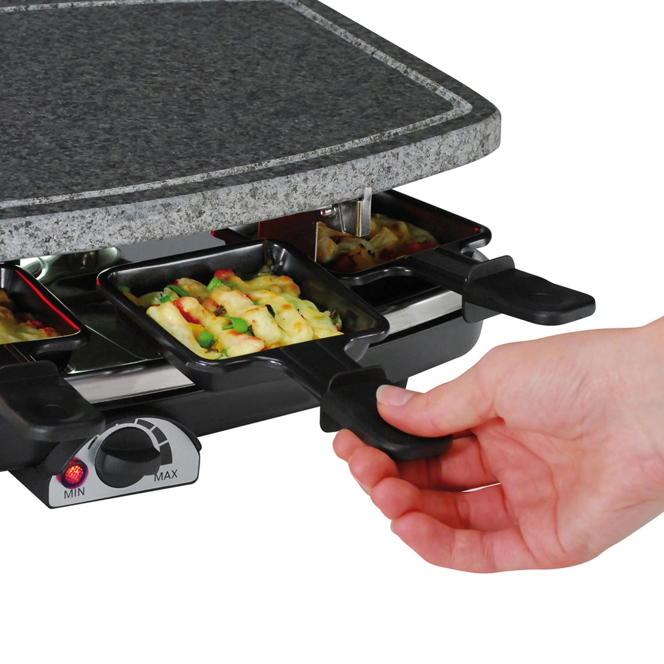 Eine Person benutzt einen Raclette-Grill mit geschmolzenem Käse und Gemüse in Pfännchen.