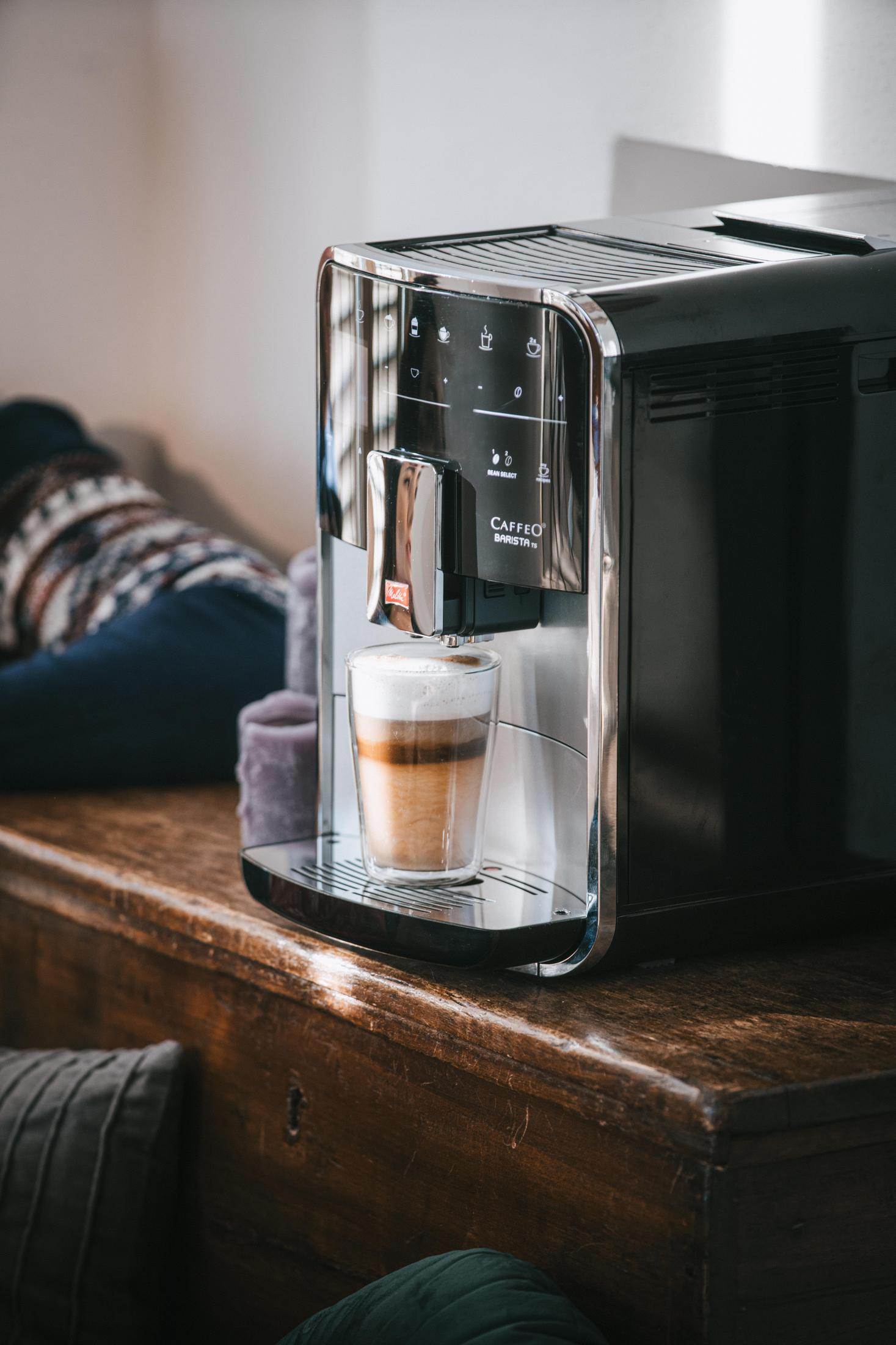 Eine schwarze Kaffeemaschine mit einem geschichteten Kaffee in einem Glas. Holz tisch, unscharfer Hintergrund.